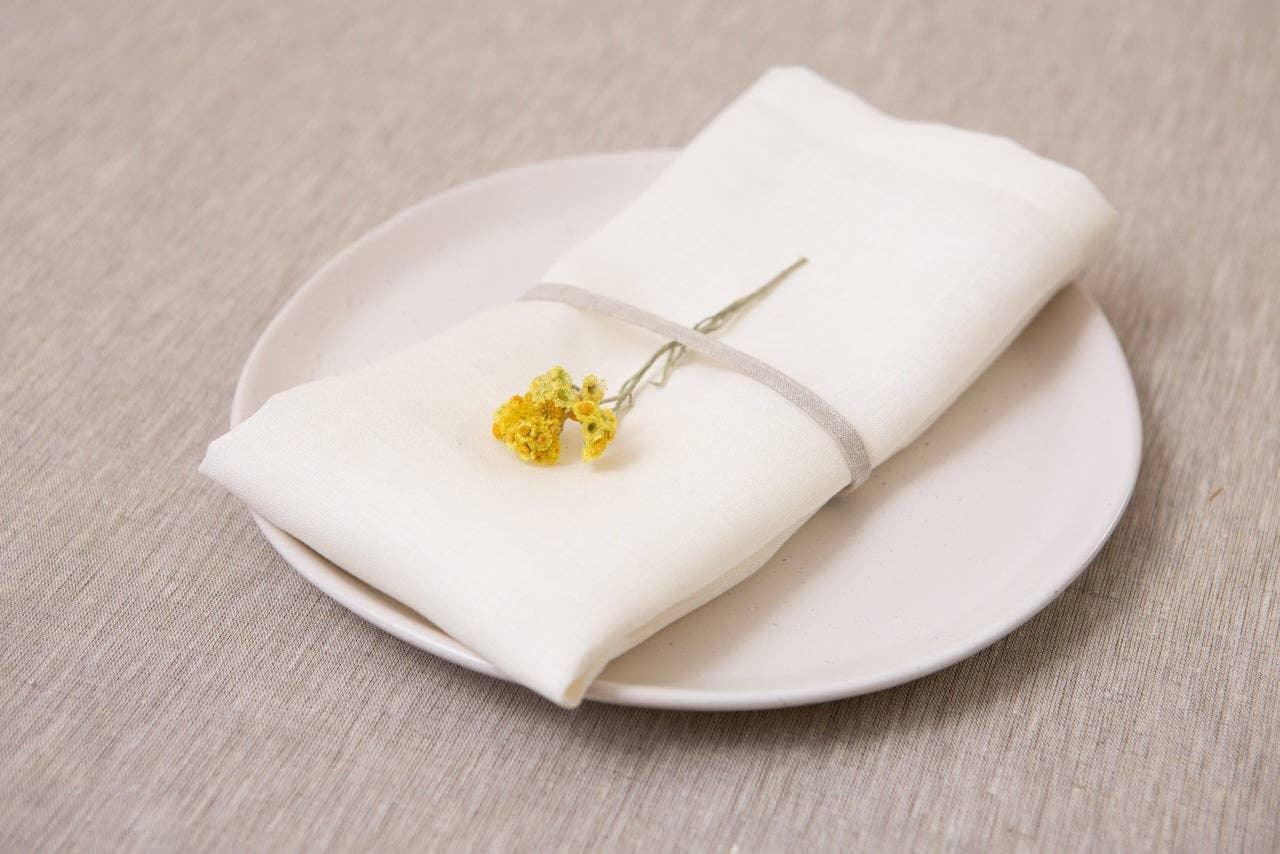 Linge Particulier linen napkin in white on ceramic plate with yellow dried flower