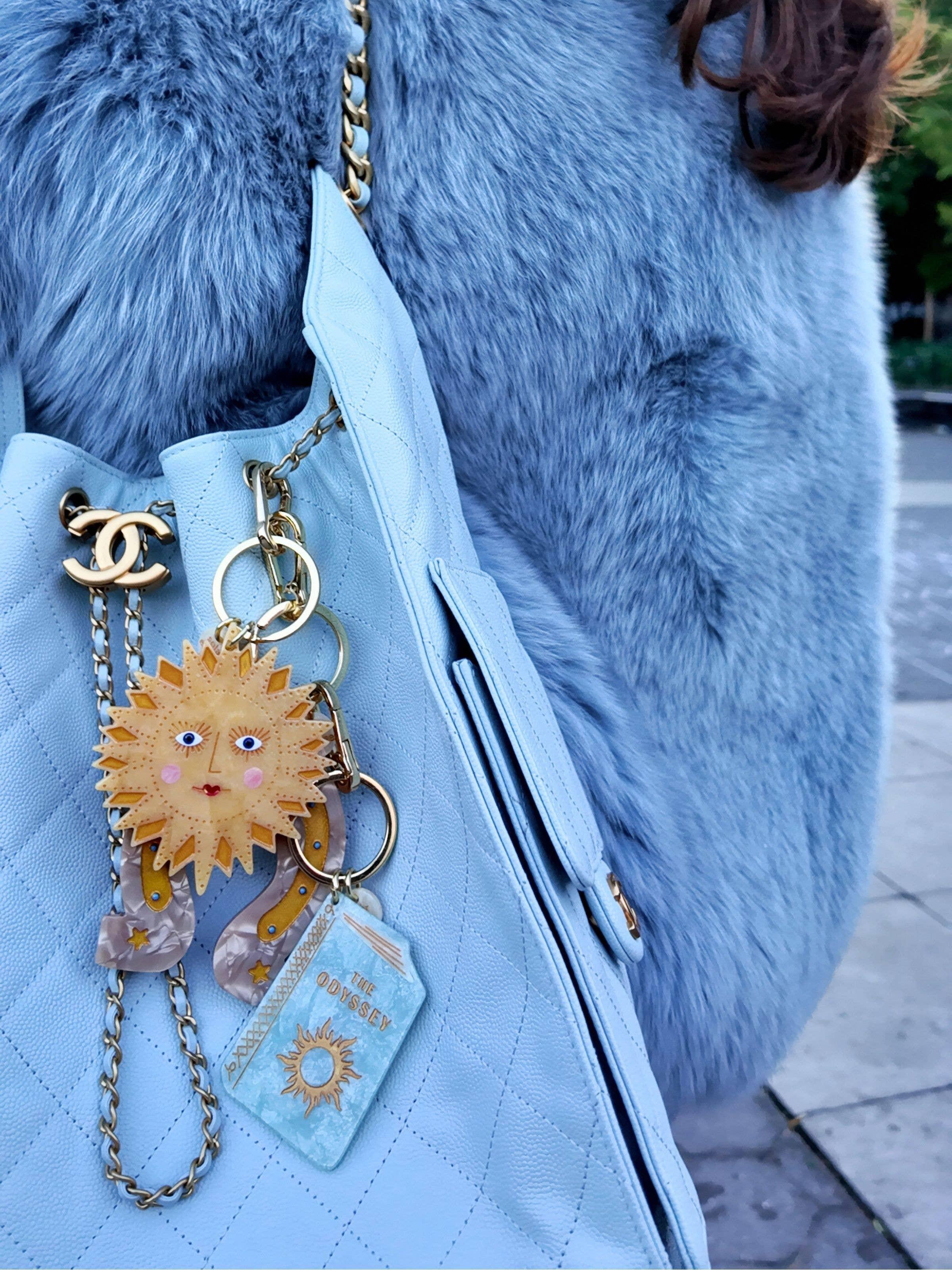 Chanel light blue leather handbag with gold chain, sun charm, and faux fur blue coat