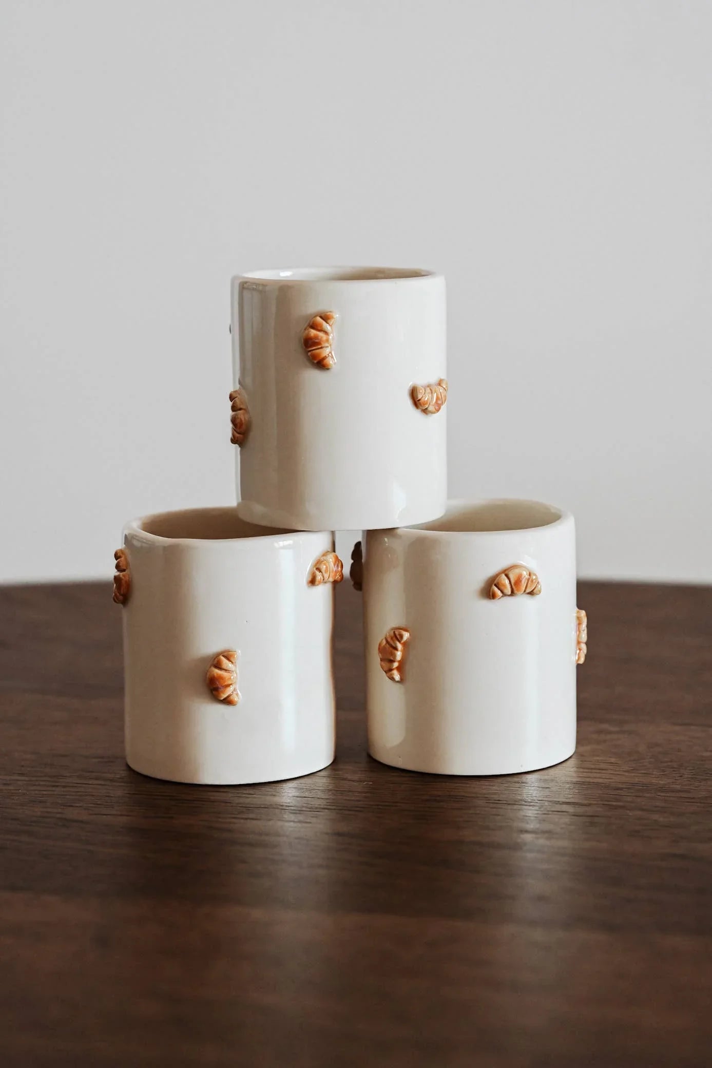 Claymates white ceramic mugs with croissant details, stacked on wooden table