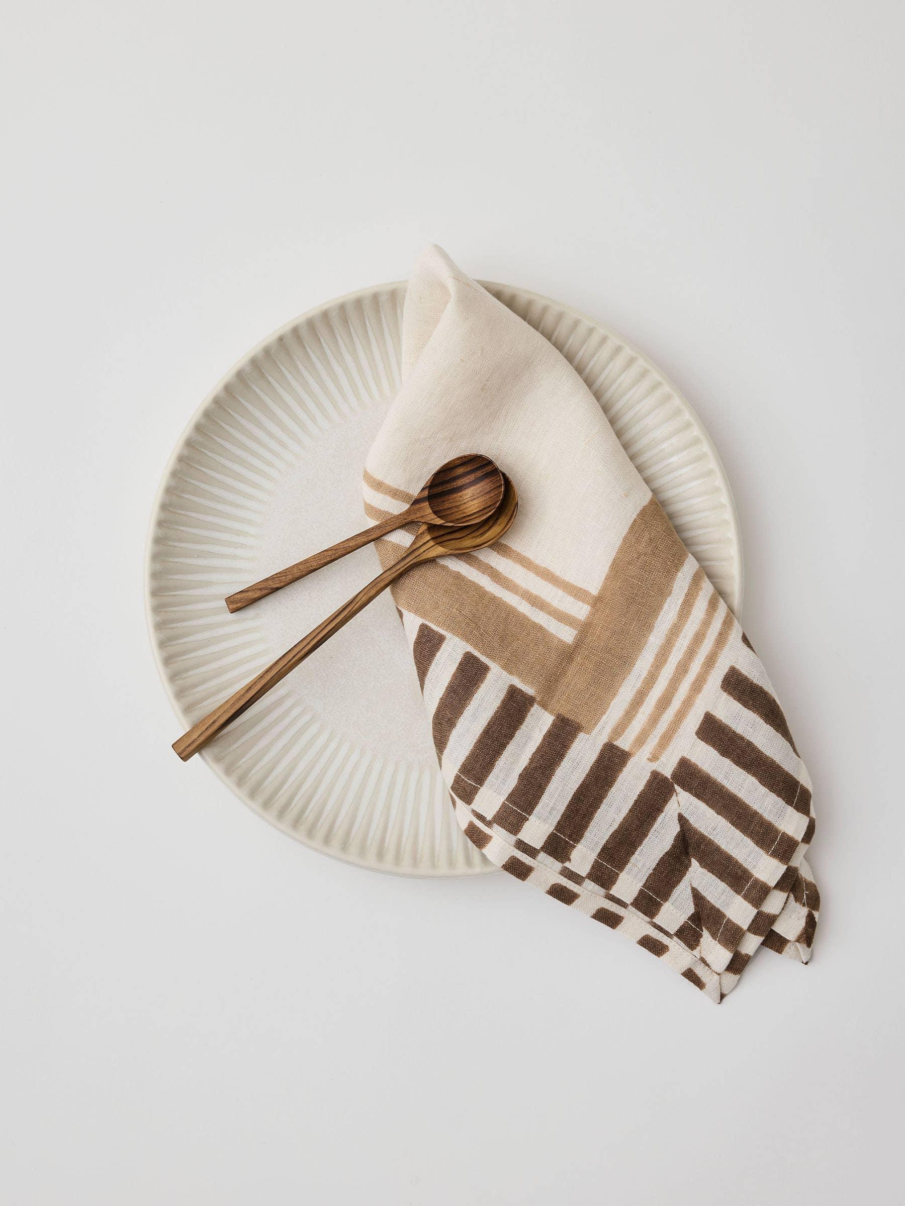 Poketo linen napkin in tan and brown on ceramic plate with wooden serving utensils