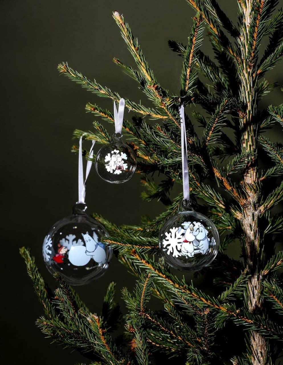Moomin glass Christmas baubles with character prints and white snowflakes hanging on pine tree