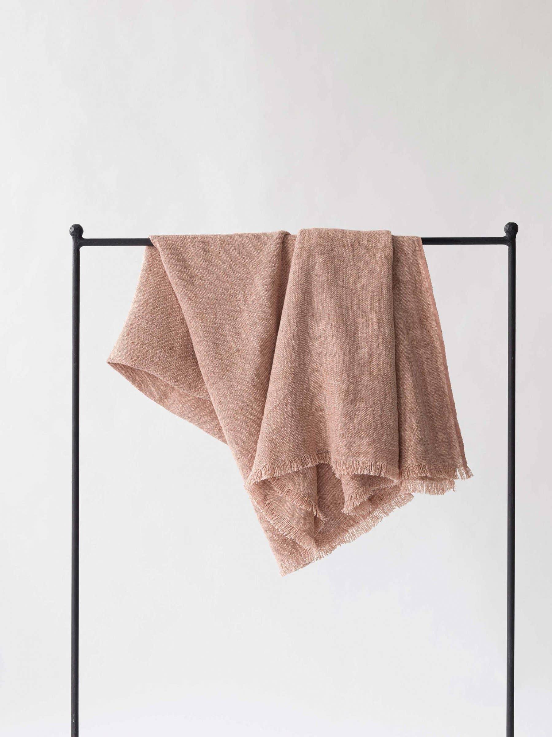 Tensira blush pink linen throw blanket with fringed edges draped on a black stand