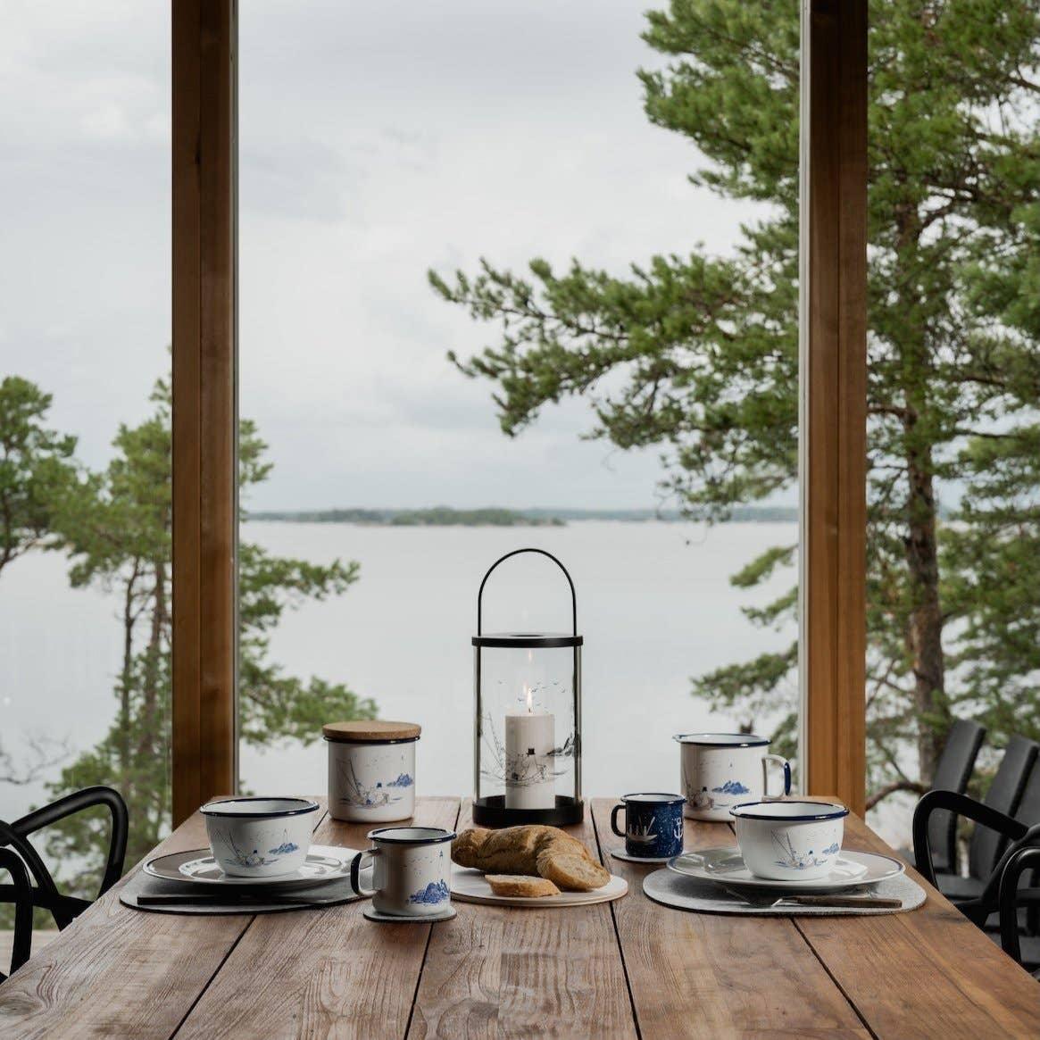 Skandinavisk porcelain mugs and bowls in blue and white on rustic wooden table, lake view