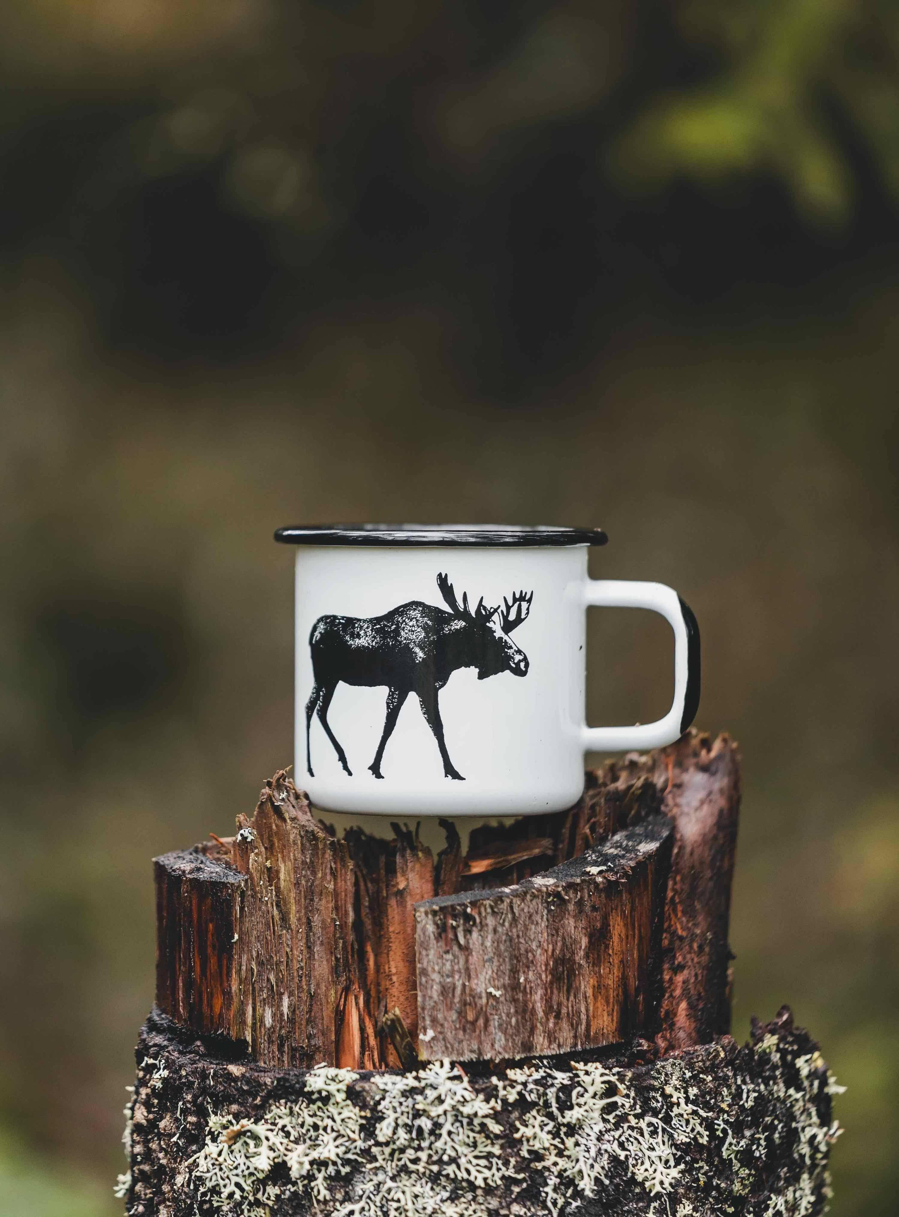 Muurla enamel mug white with black moose print, outdoors on tree stump