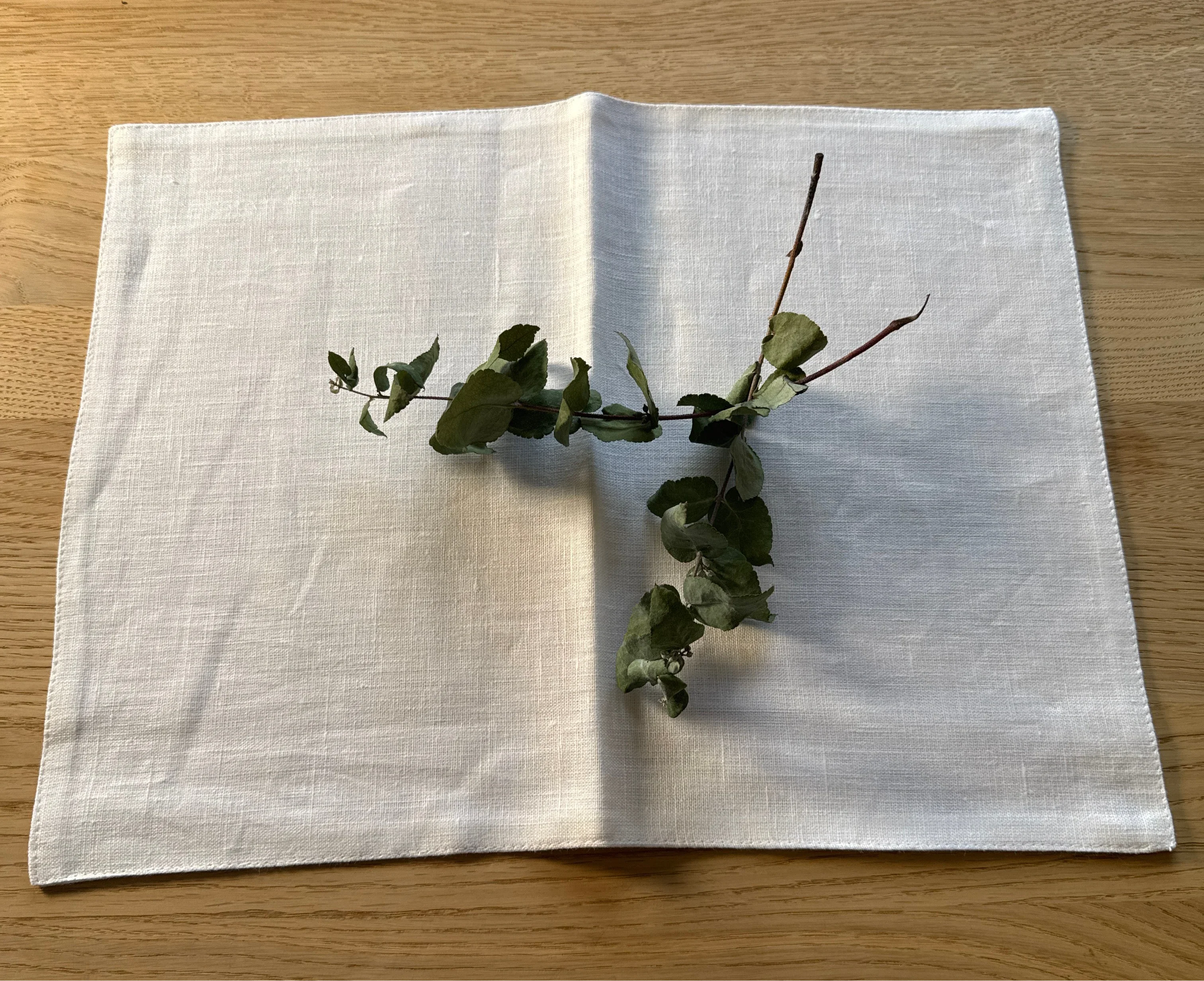 RIG-TIG white linen napkin on wood table with green botanical decoration