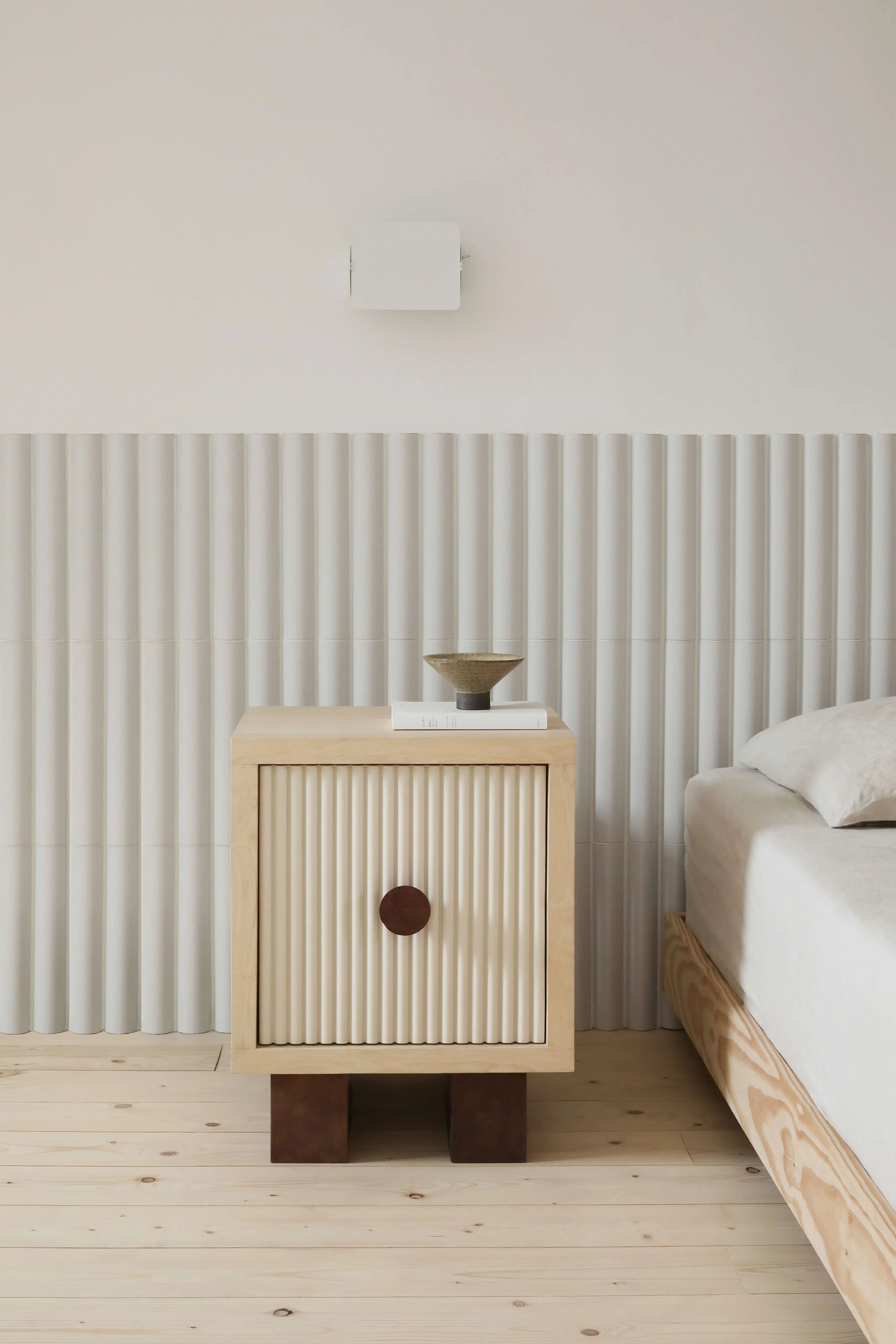 Heju x Nobodinoz bedside table in light wood and cream, beside a minimalist bed