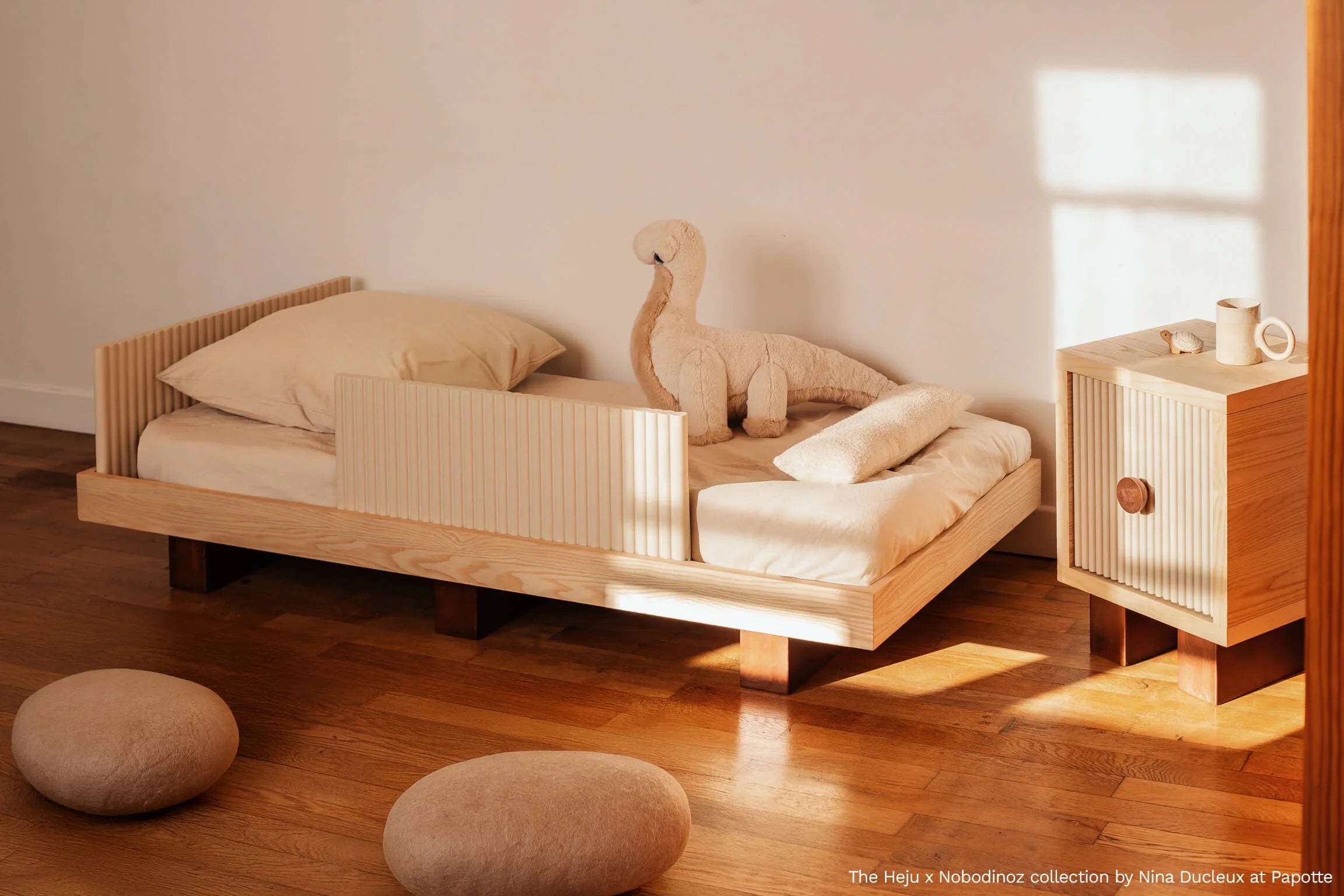 Heju x Nobodinoz wooden bedside table with ribbed front, light wood finish, in a sunlit room