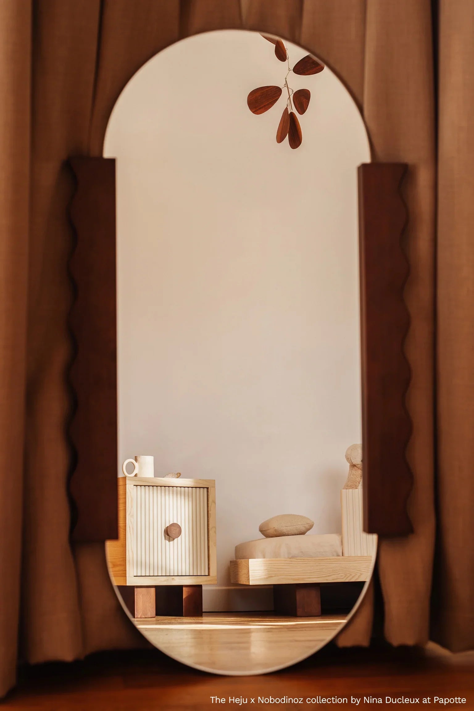Heju x Nobodinoz arched wood mirror with neutral tones, set against beige curtains