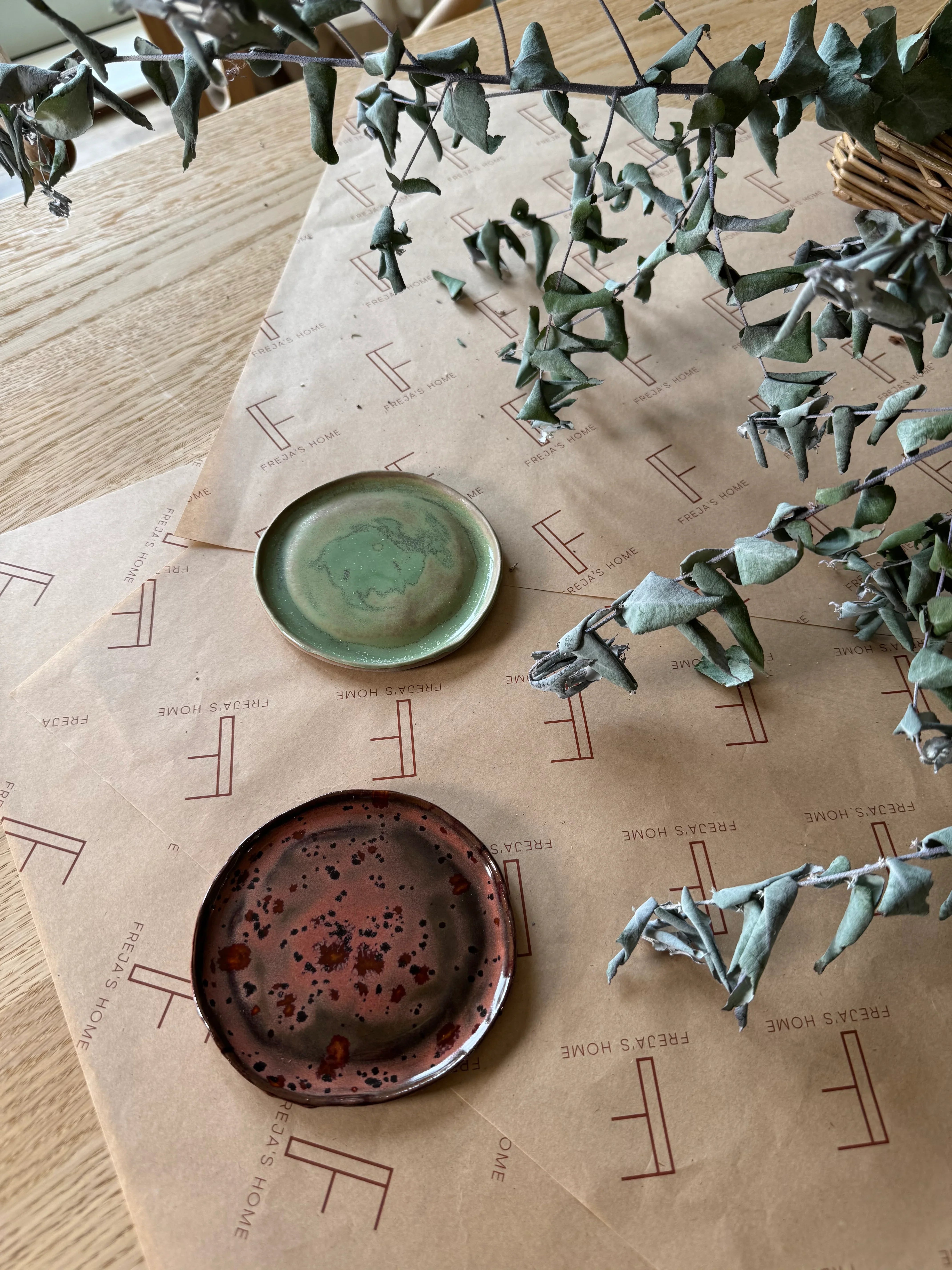 Freja's Home ceramic plates in green and brown on branded paper with dried leaves