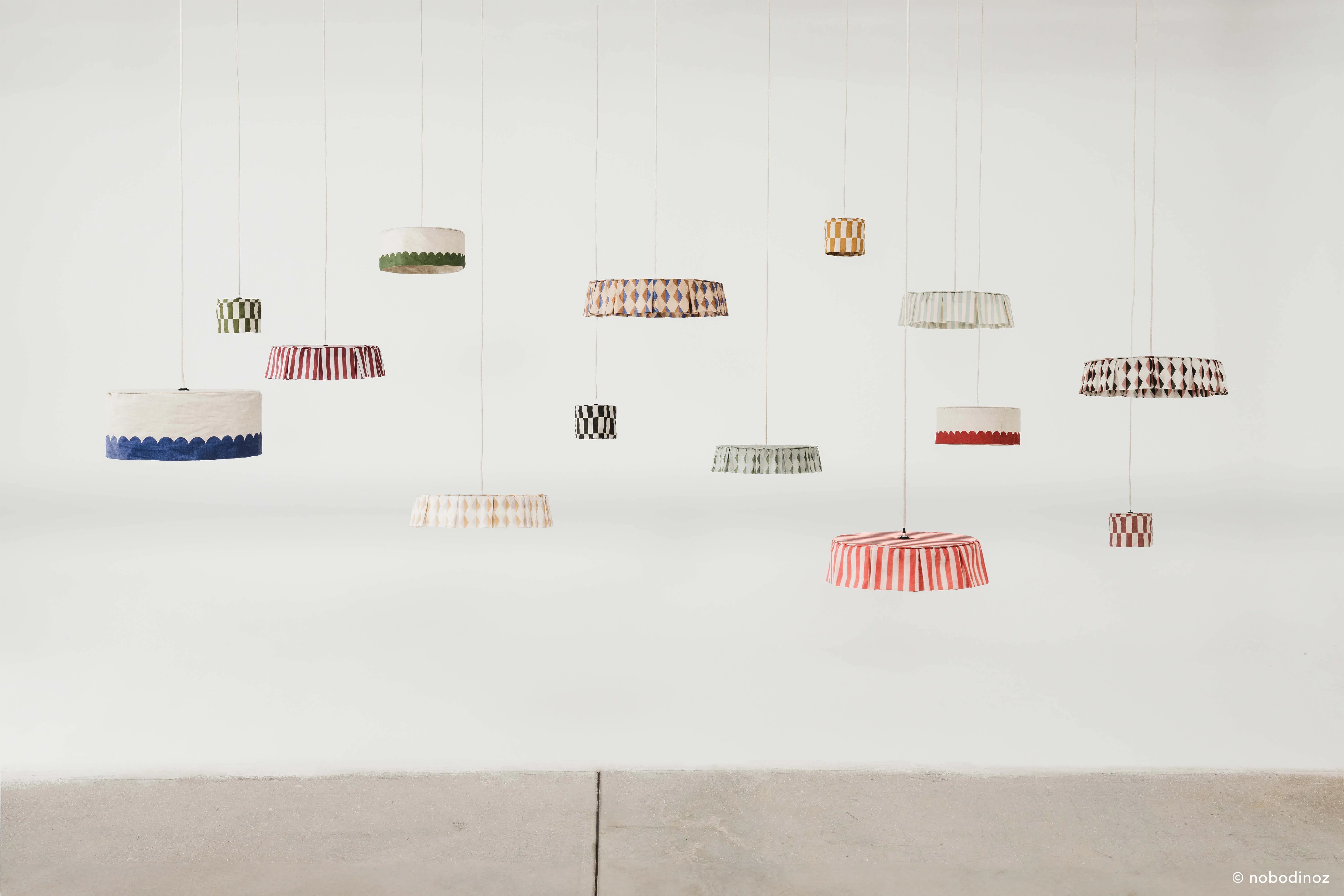 Nobodinoz premium linen lampshades in assorted colours and patterns, hanging display.