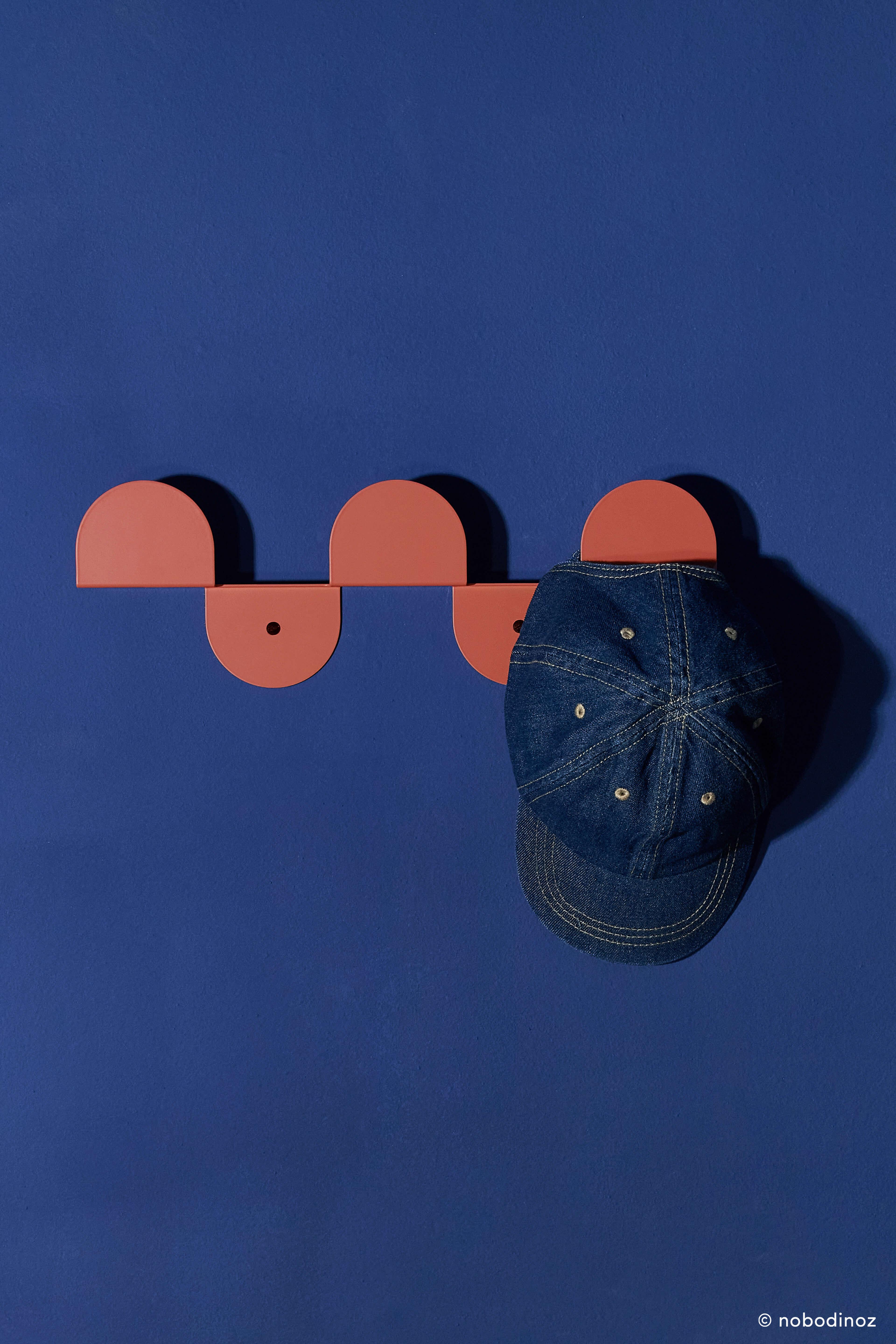 Nobodinoz burnt red steel wall coat rack with denim cap on blue wall