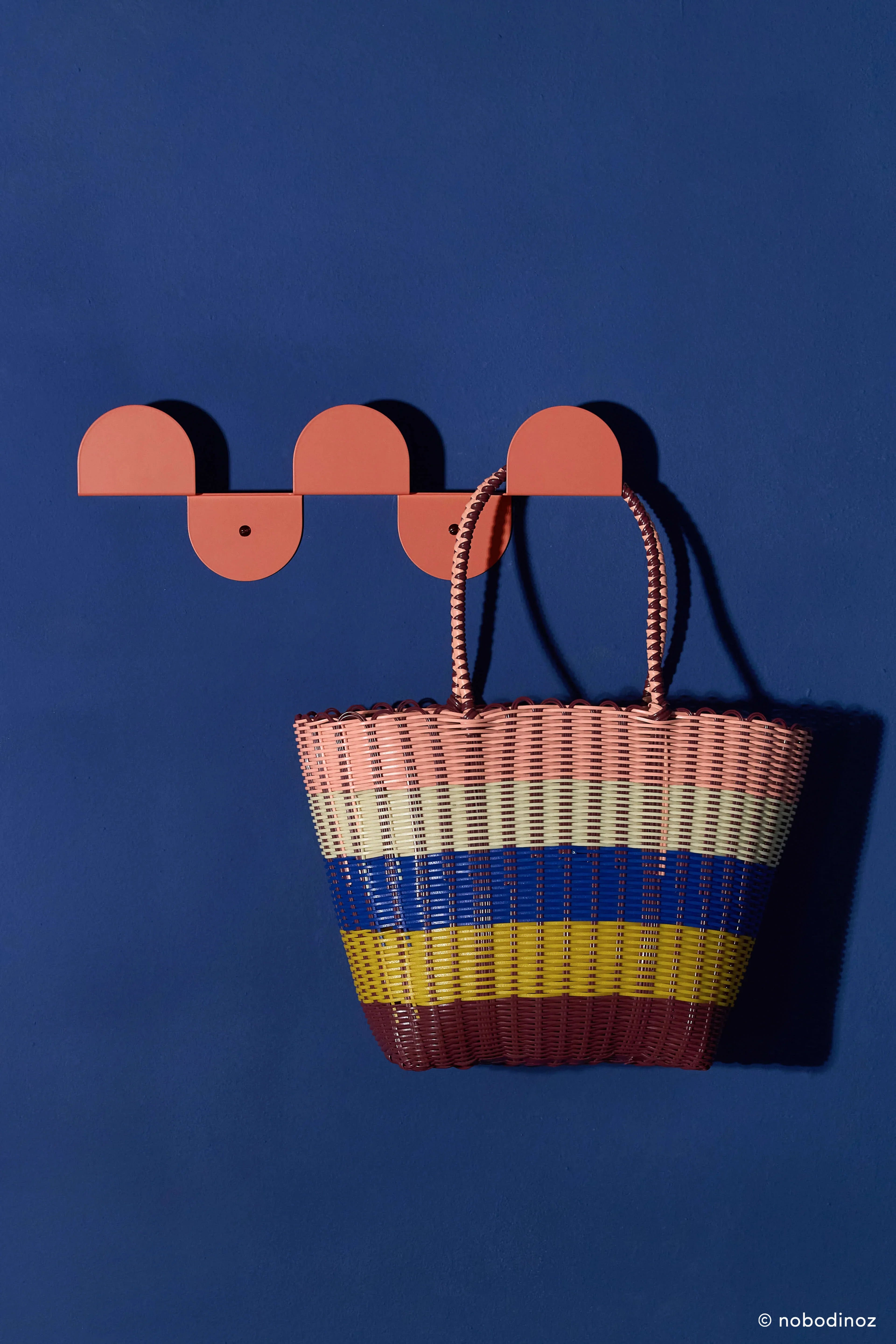 Nobodinoz burnt red steel wall coat rack with colorful woven bag on blue wall