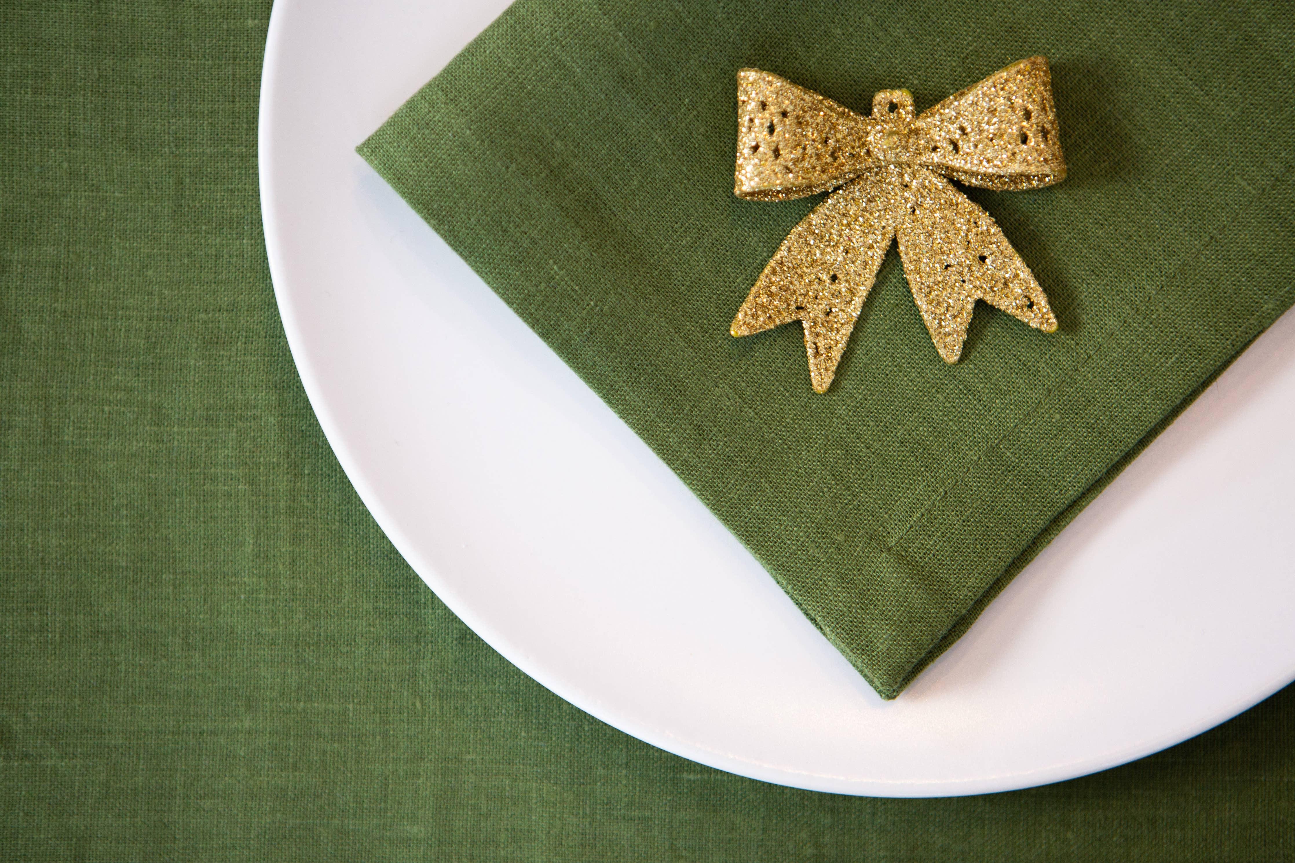 Maison Tess green linen napkin on white plate with gold glitter bow accent