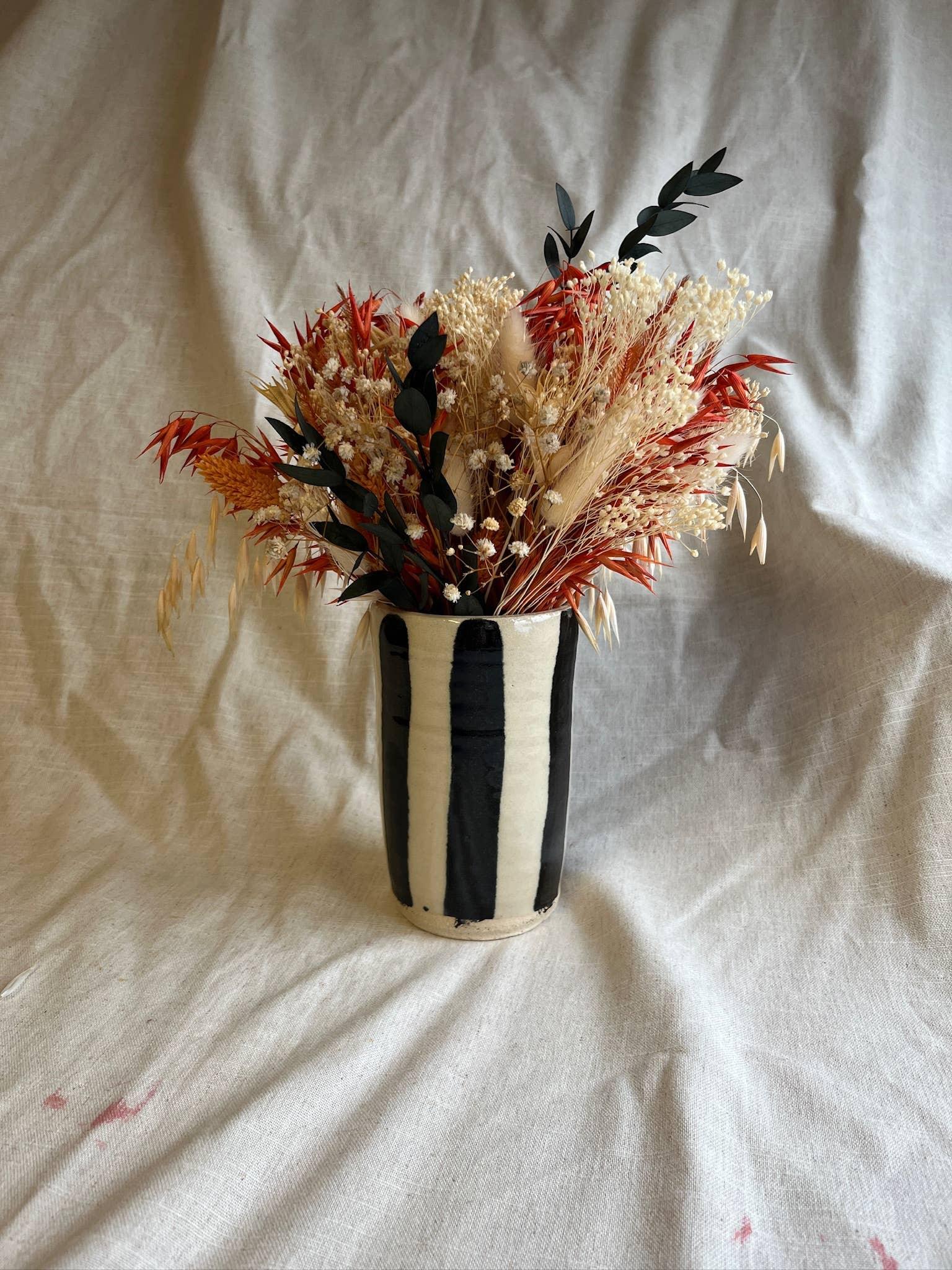 Striped ceramic vase with dried flowers and grasses in cream, black, red and beige tones.