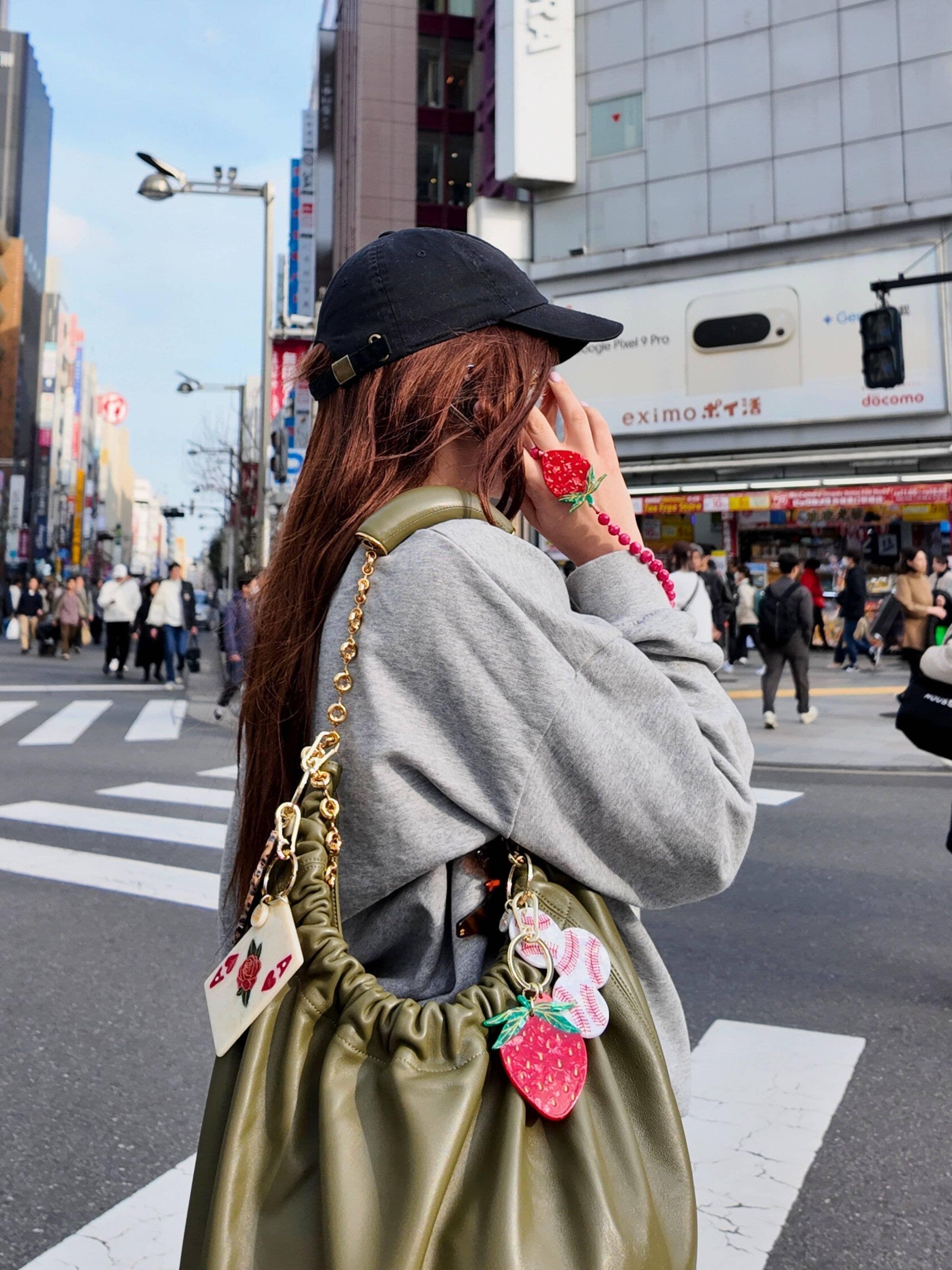Casual street style with olive leather bag featuring gold chain, playful charms, city background