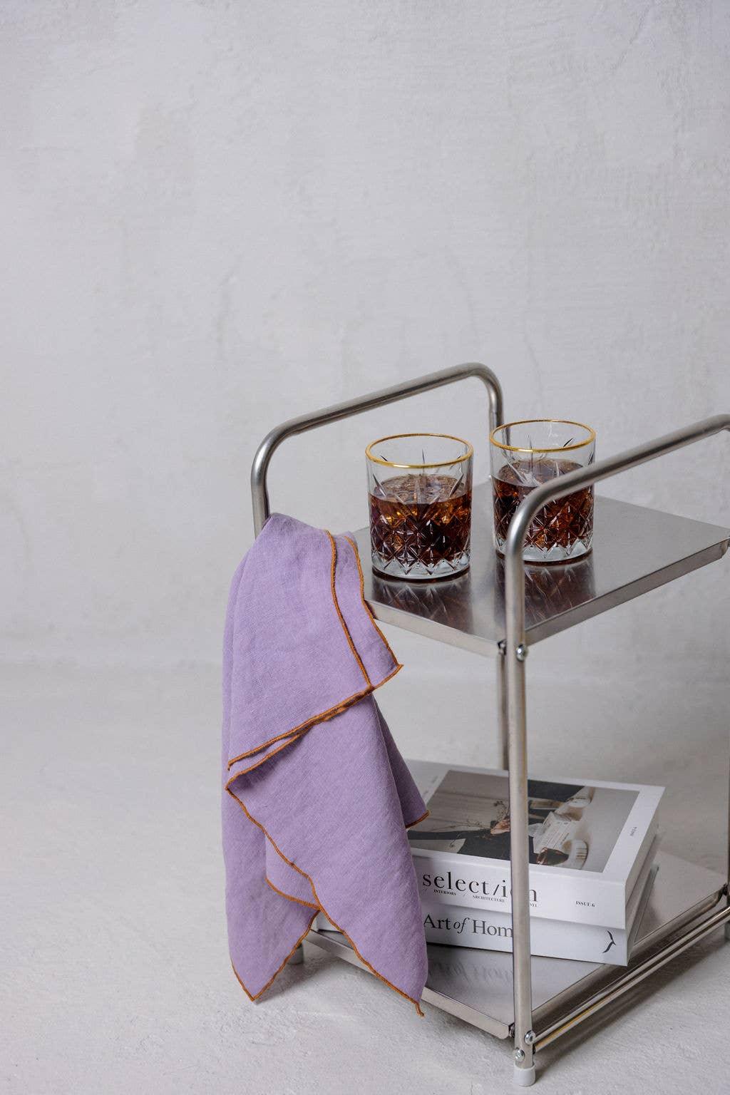 MADE BY YOKE steel bar cart with two crystal glasses, lilac linen napkin, and books