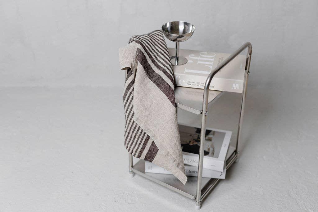 Minimalist stainless steel side table with striped linen towel, silver bowl, and neutral books