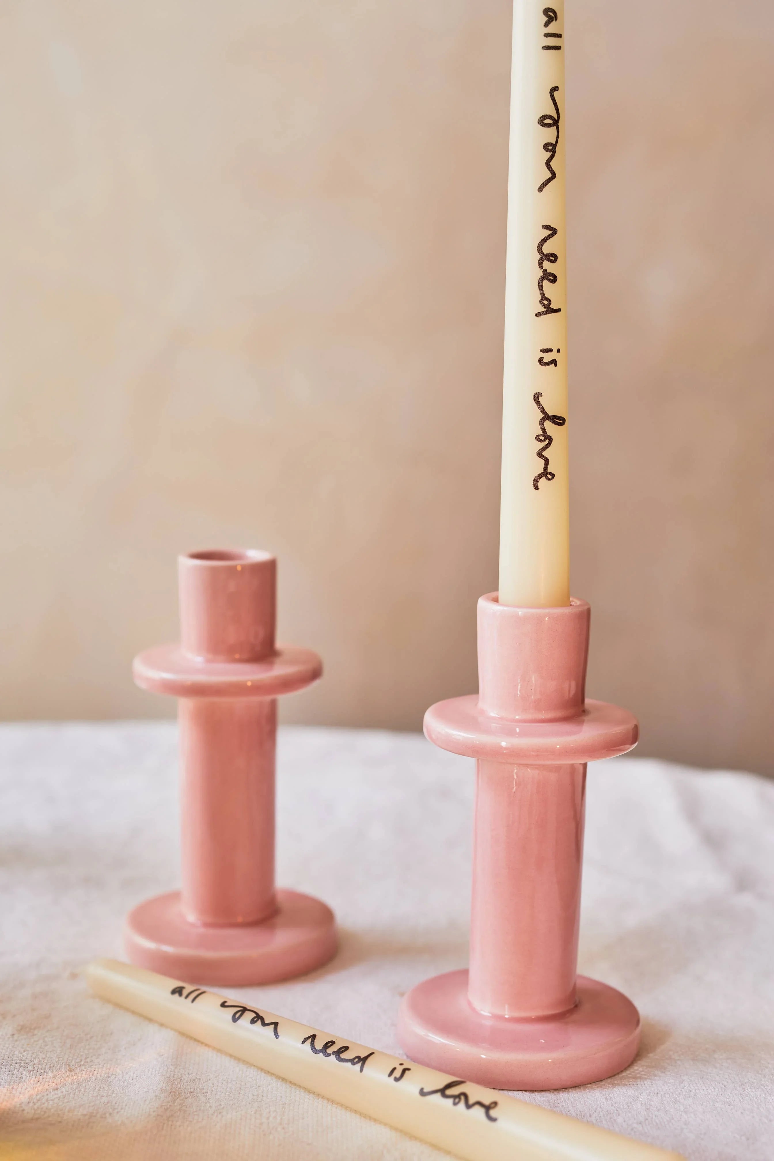 OYOY ceramic pink candle holders with cream taper candle, 'all you need is love' text