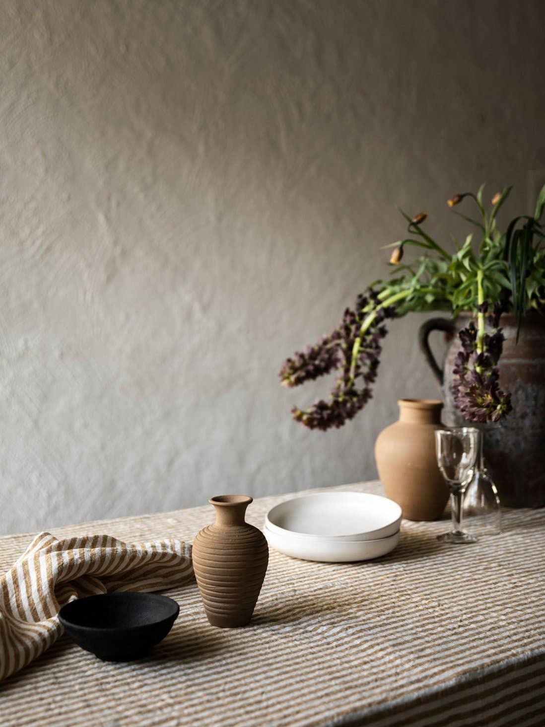 Handcrafted Hasami ceramic vases and bowls in natural brown and black on a striped tablecloth