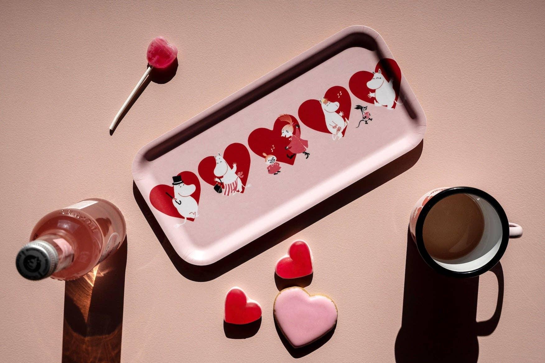 Moomin pink melamine tray with red heart designs, mugs, and heart-shaped cookies on a blush surface