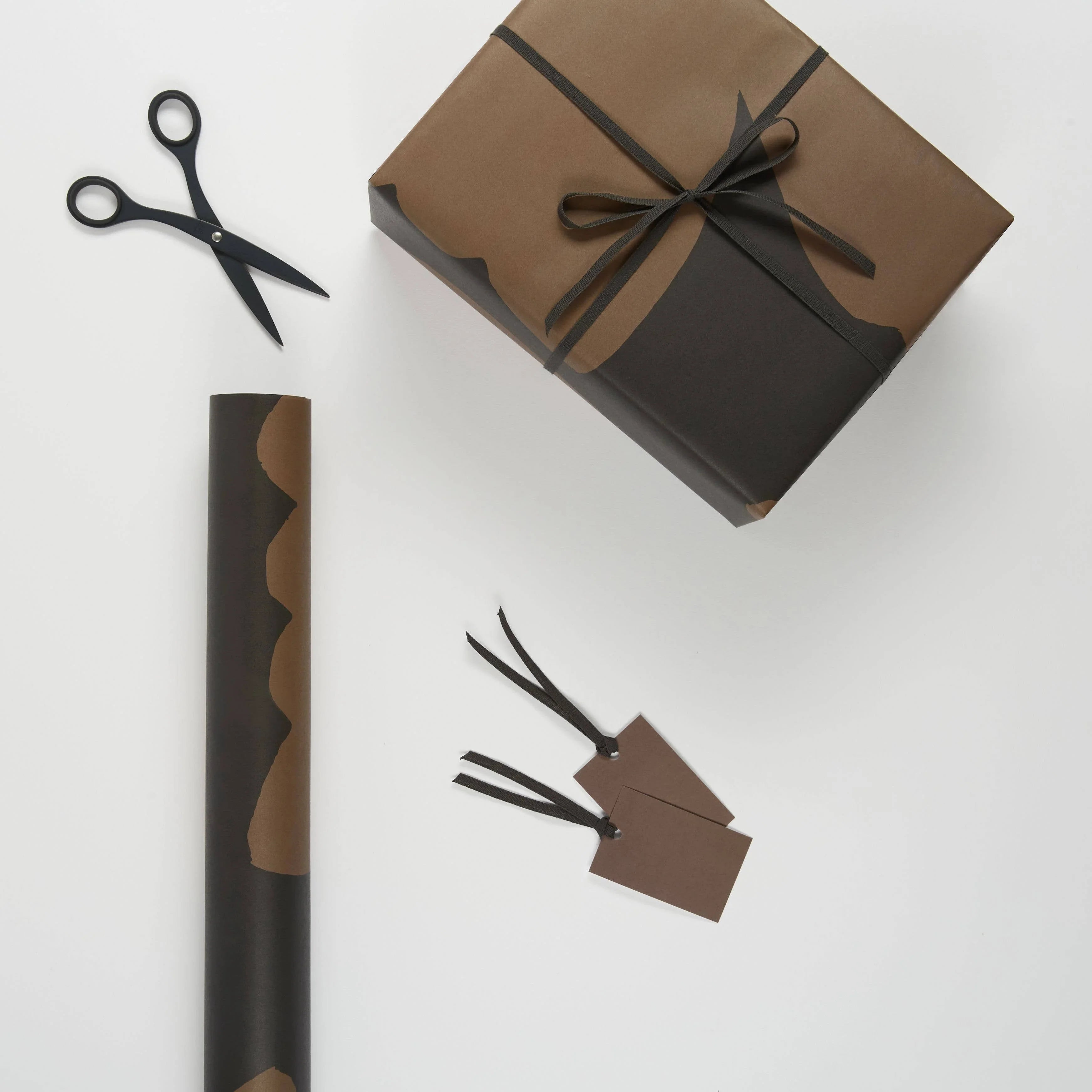 Monographie brown and black gift wrapping paper, scissors, and tags on white background