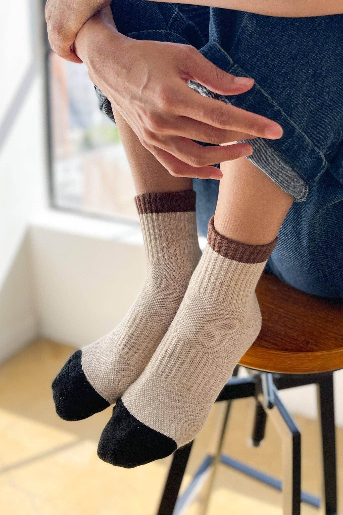 HAVN crew socks in beige cotton with brown cuffs and black toes, worn indoors