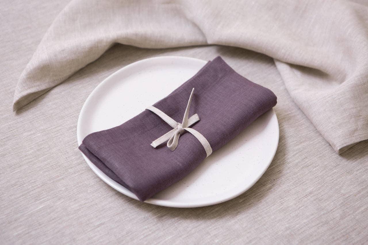 Linge Particulars linen napkin in plum on white plate, beige linen tablecloth