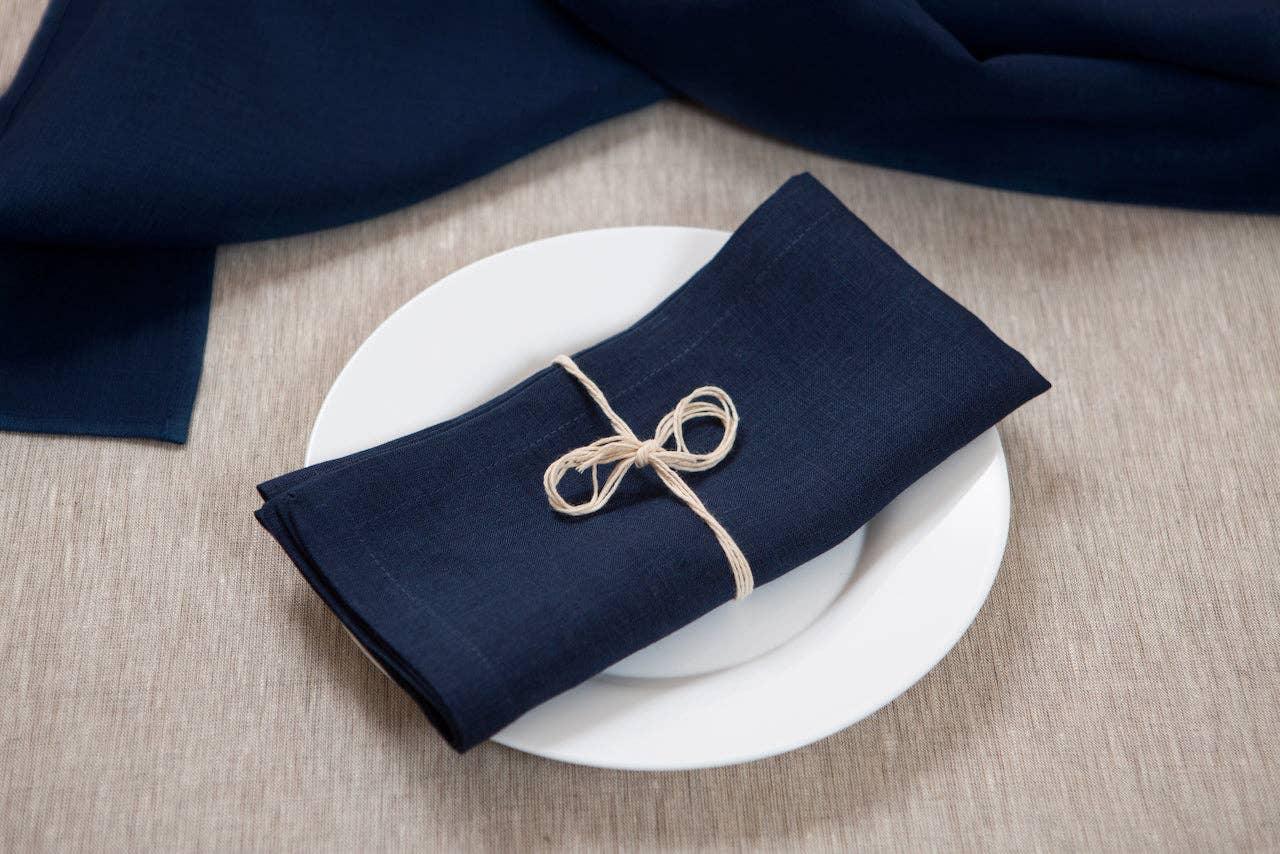 LinenCasa navy linen napkin on white plate, tied with twine, on neutral tablecloth.