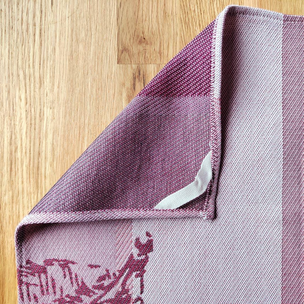 Studio Leoni woven cotton tea towel in purple and pink tones on wooden surface