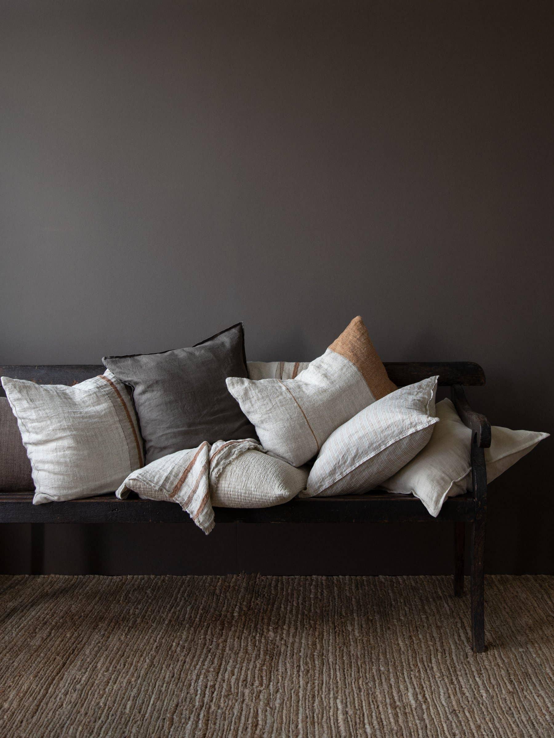 de Le Cuona linen and wool cushions in neutral tones on a dark wood bench