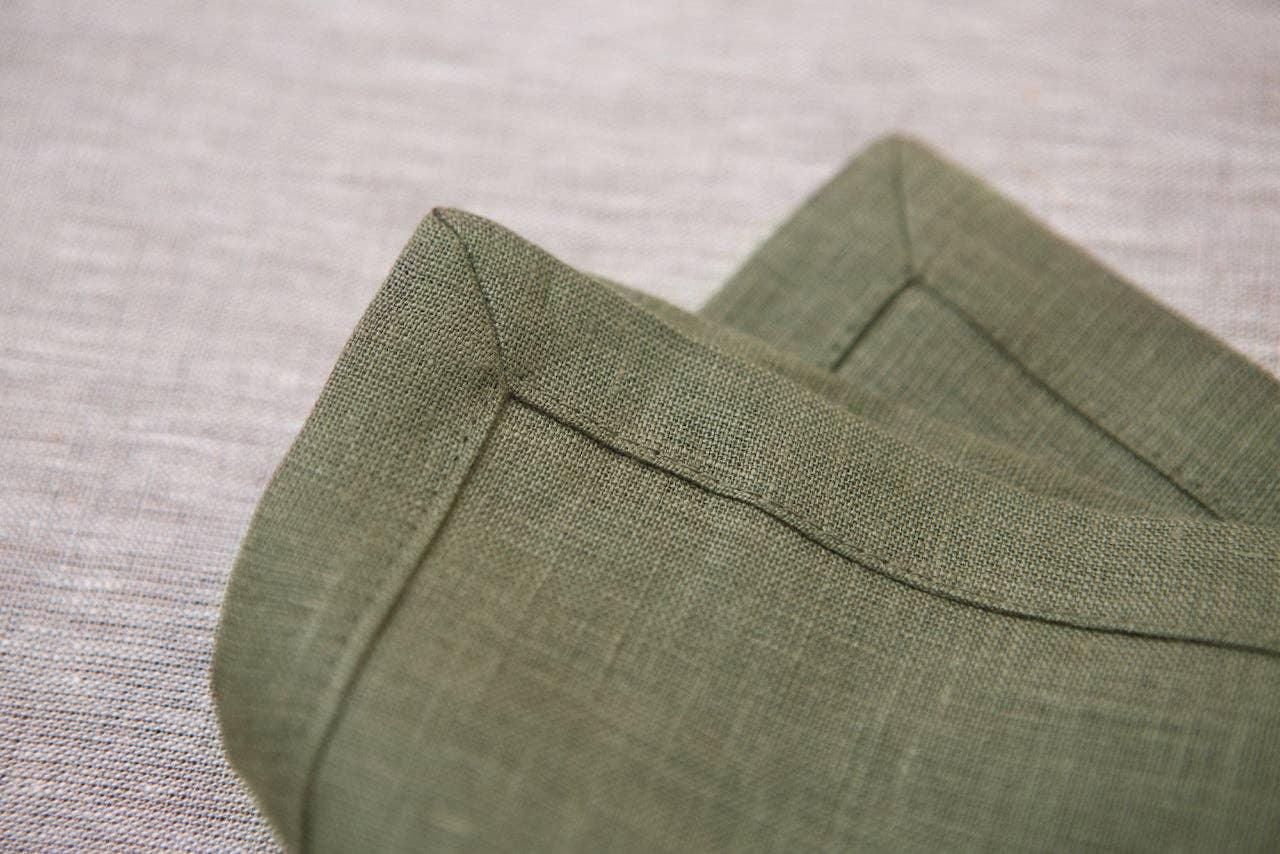 MagicLinen olive green linen napkin with mitred corners on a neutral tablecloth