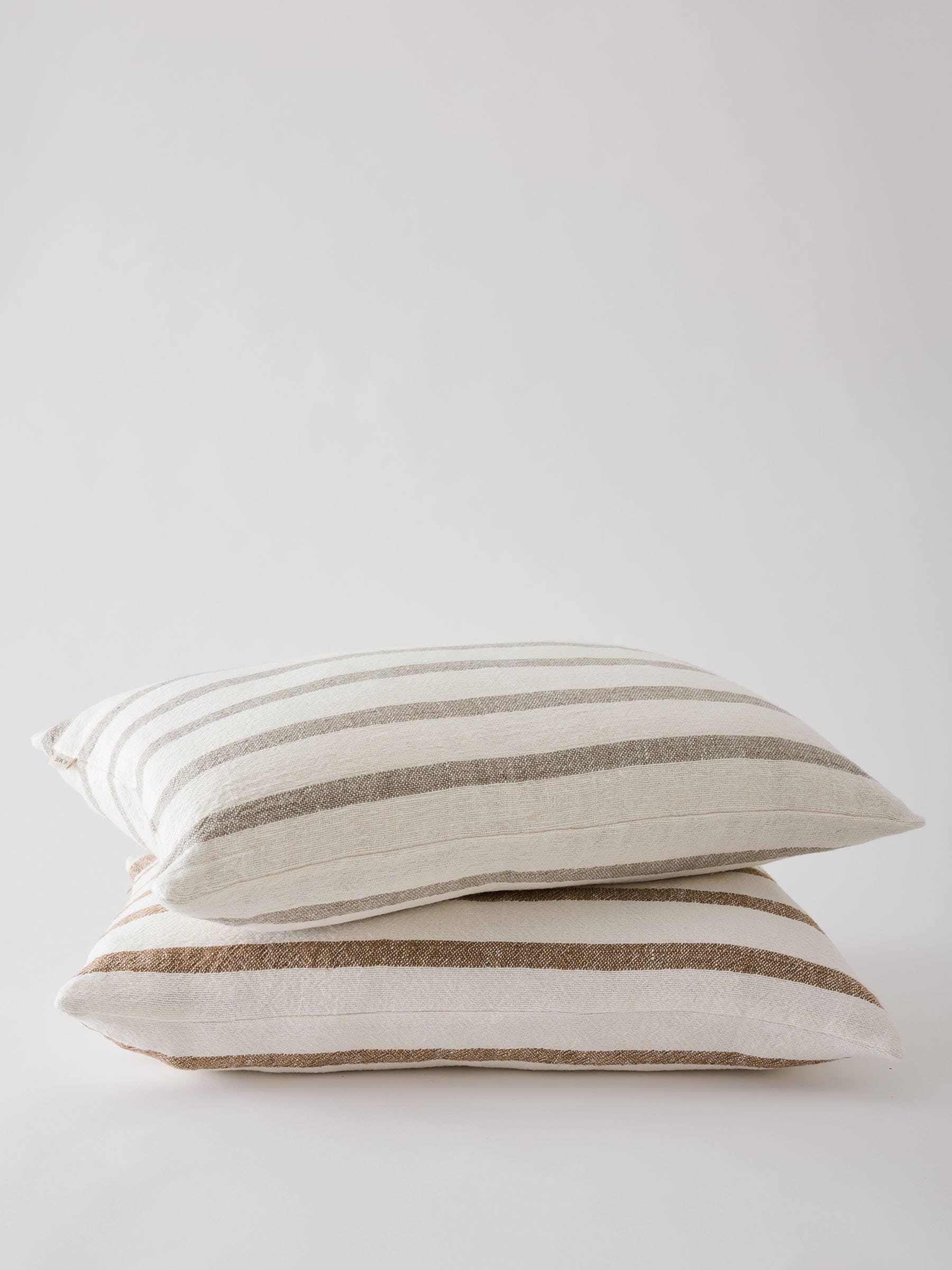 Two Cultiver linen striped pillows in beige and white stacked on a white background
