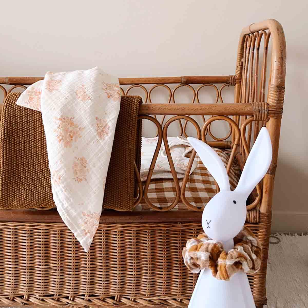 Olli Ella rattan crib with brown knit blanket, floral muslin, and white bunny decor