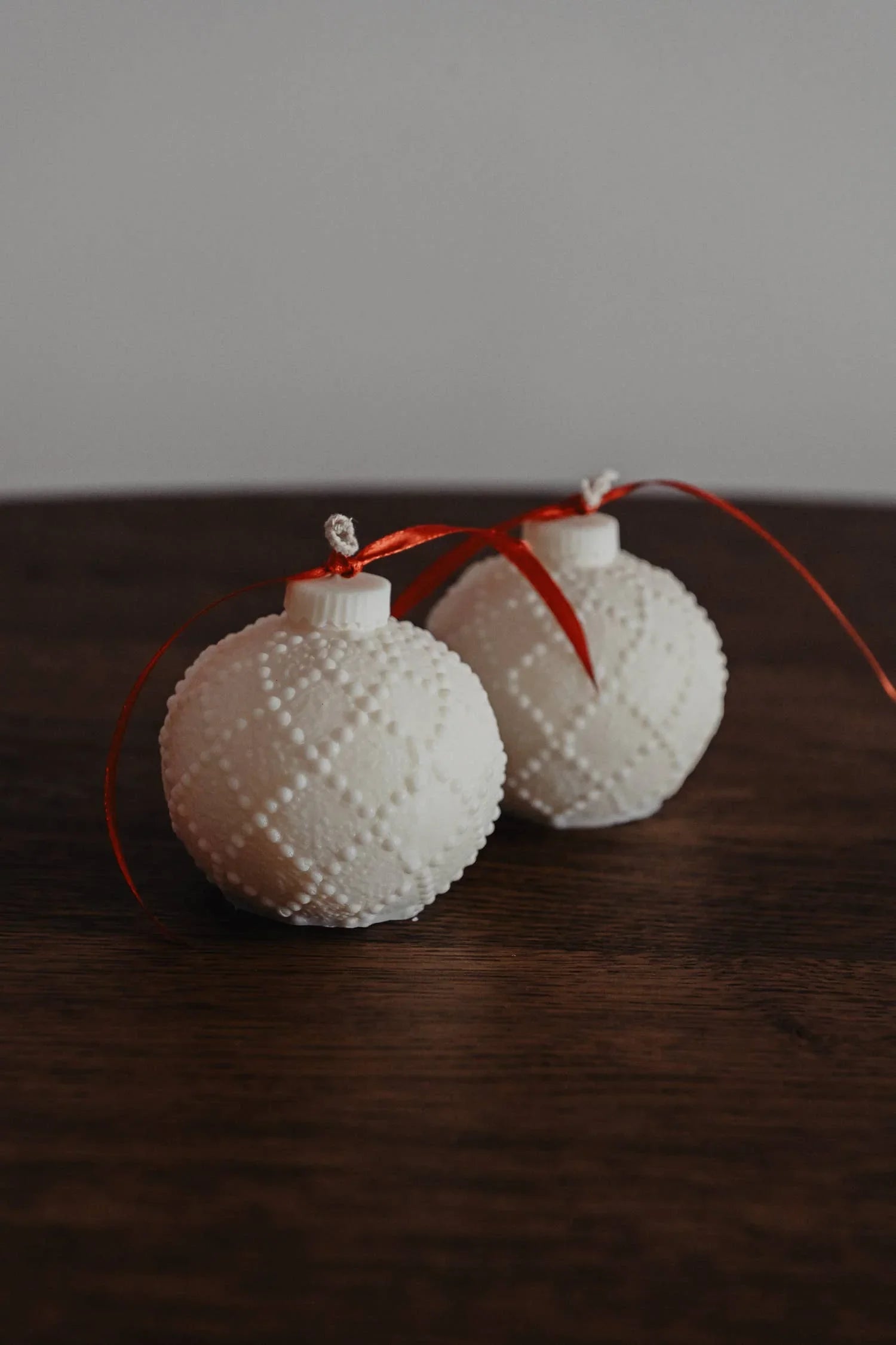 VIBAe textured white ceramic Christmas ornaments with red ribbon on dark wood
