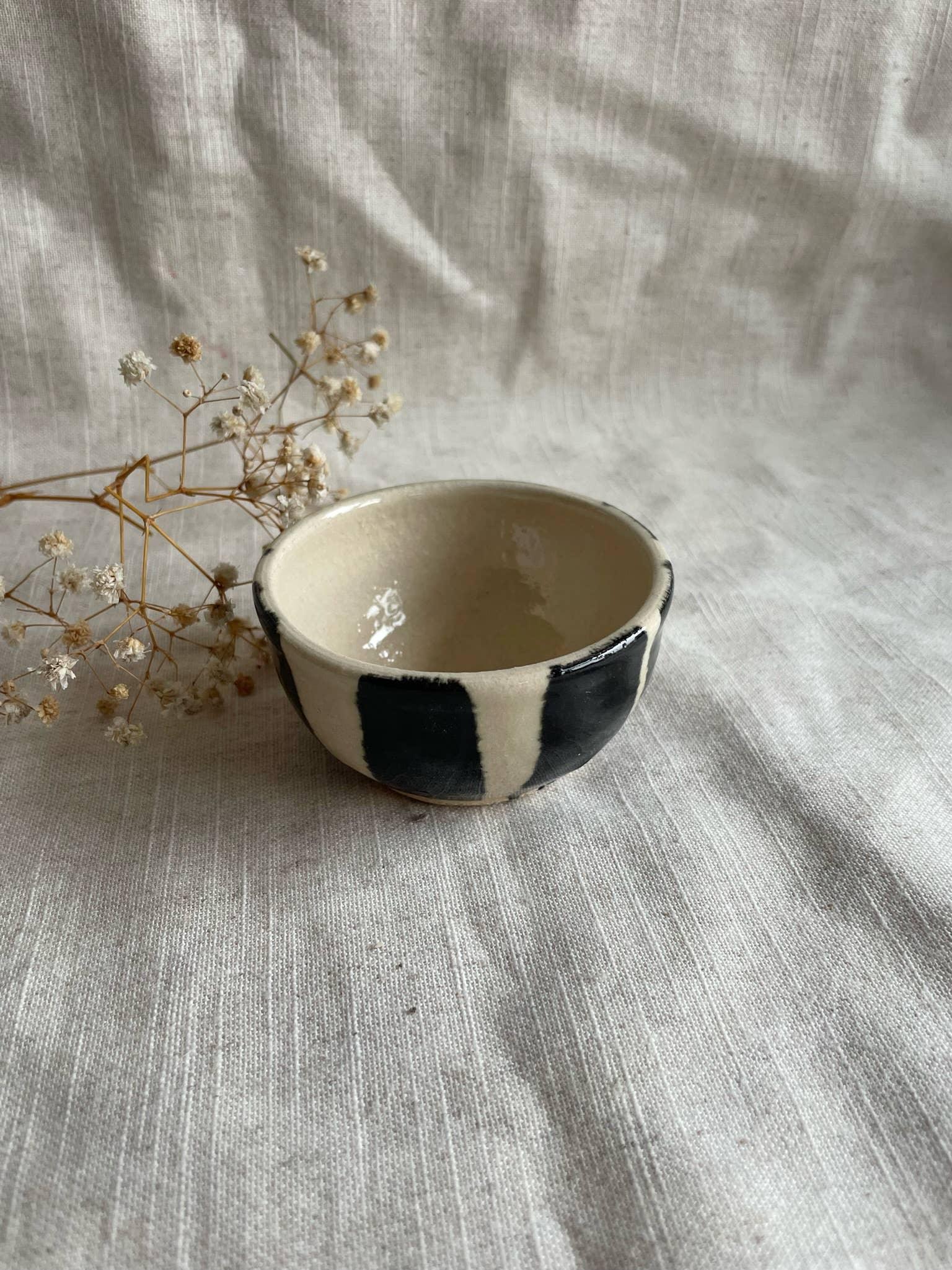 Handcrafted ceramic bowl with black and white glaze on linen, dried flowers beside