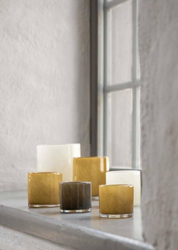 Ferm Living glass tealight holders in amber, brown, and white on a windowsill