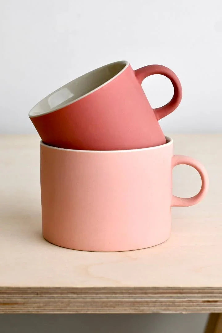 Yield Design ceramic mugs in pink and coral, minimalist style on wood surface