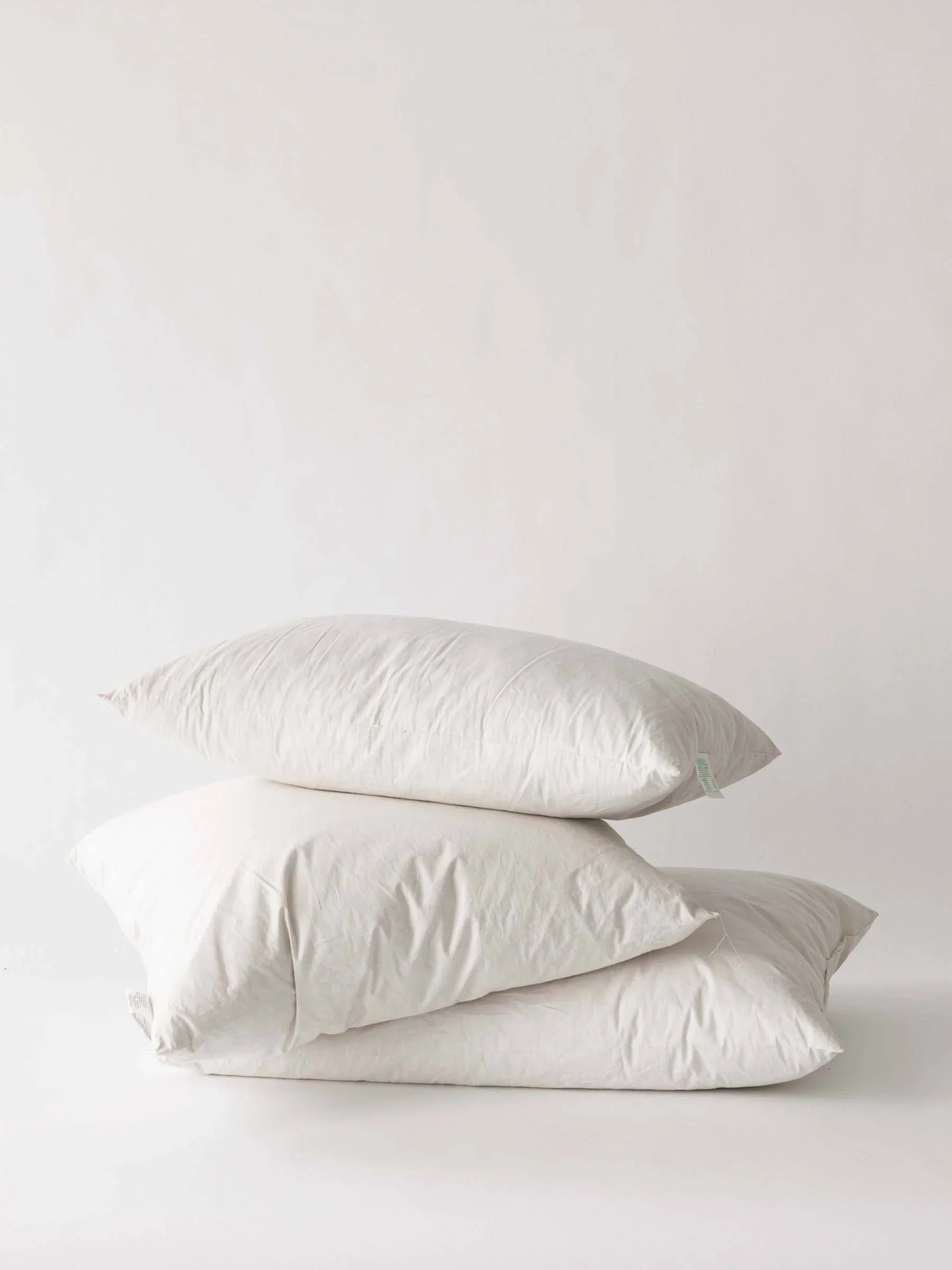 Three FluffCo white cotton bed pillows stacked on a minimalist white background