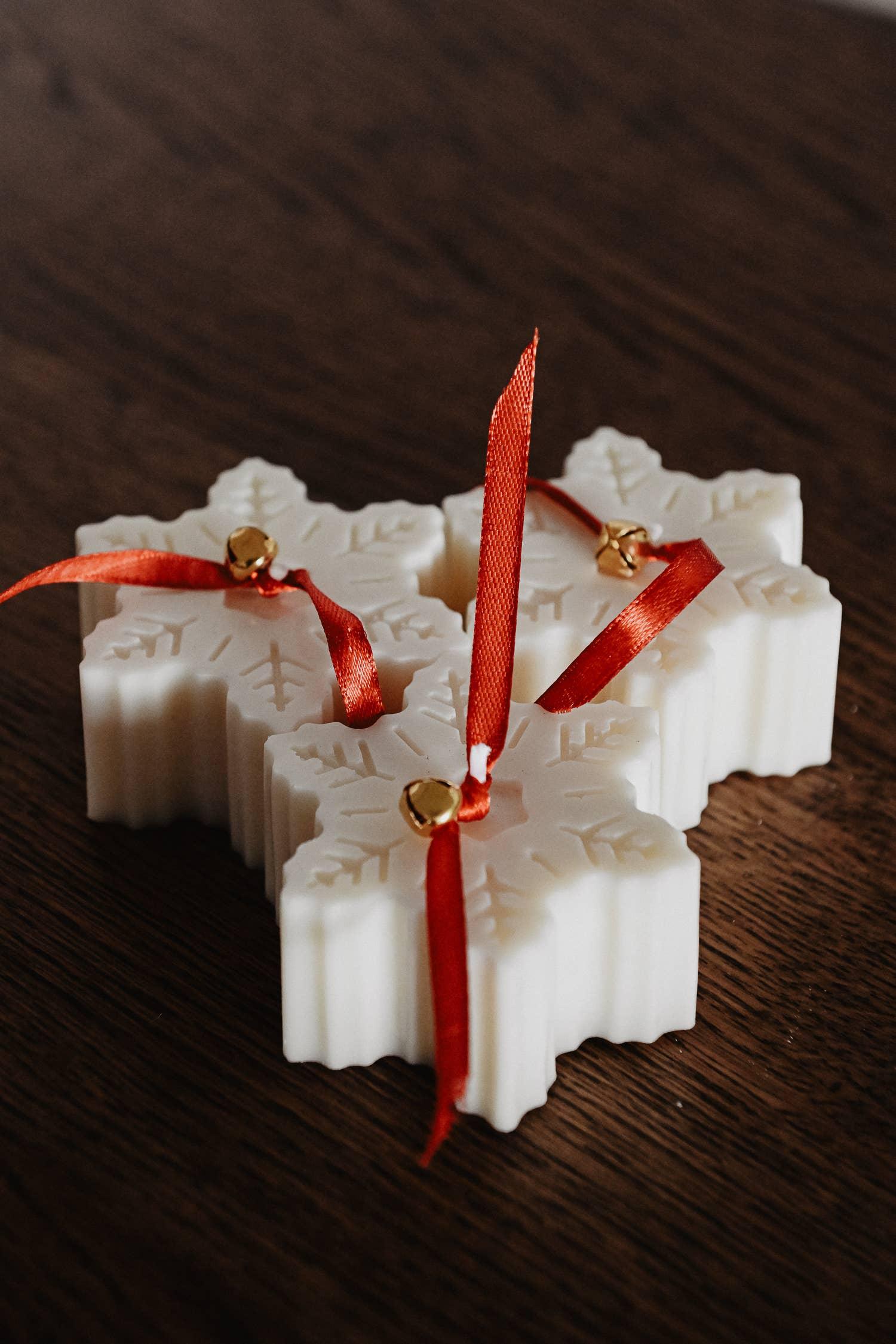 White snowflake-shaped candles with red ribbons and gold bells on a wooden table.