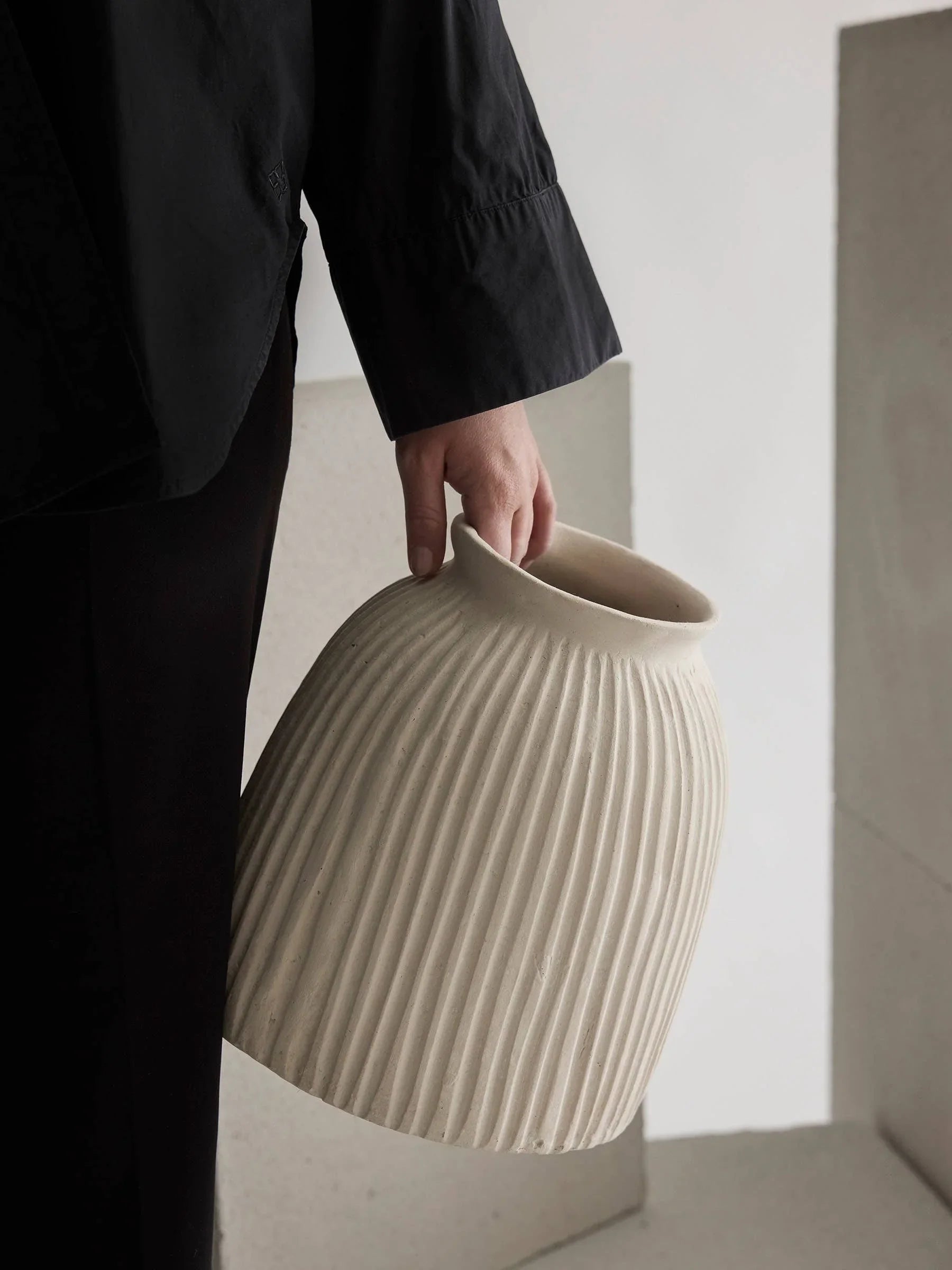 KLAY Studio cream ceramic fluted vase held by person in black clothing, minimalist setting