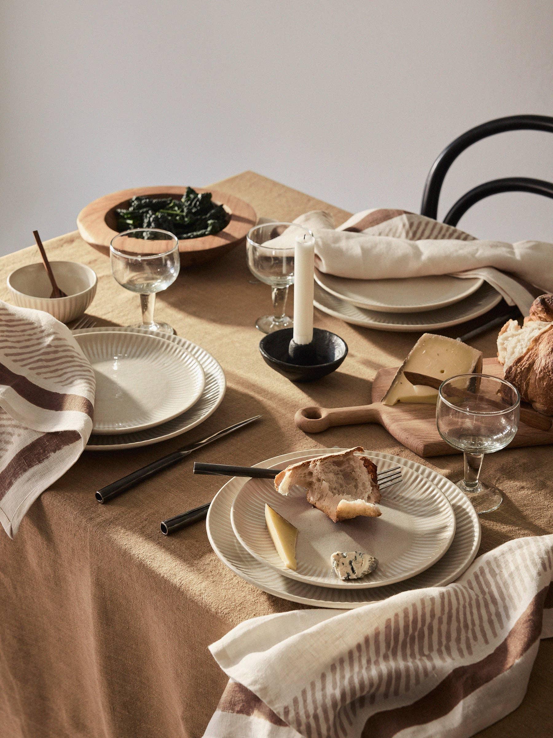 Feldspar ceramic plates and bowls in cream, set on a beige linen tablecloth with glassware.