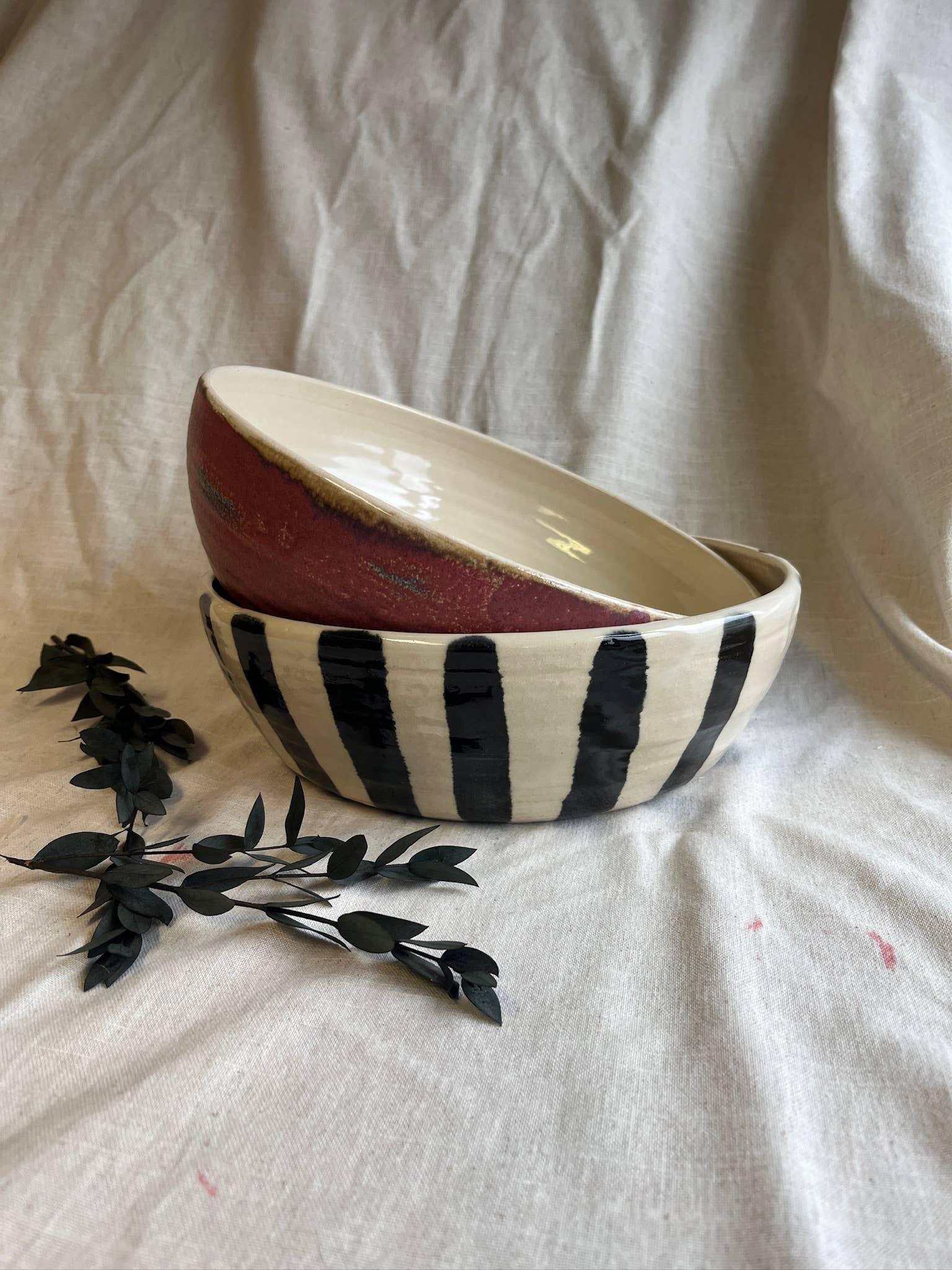 Livity premium handmade ceramic bowls, one in red and cream and one with black stripes, on fabric