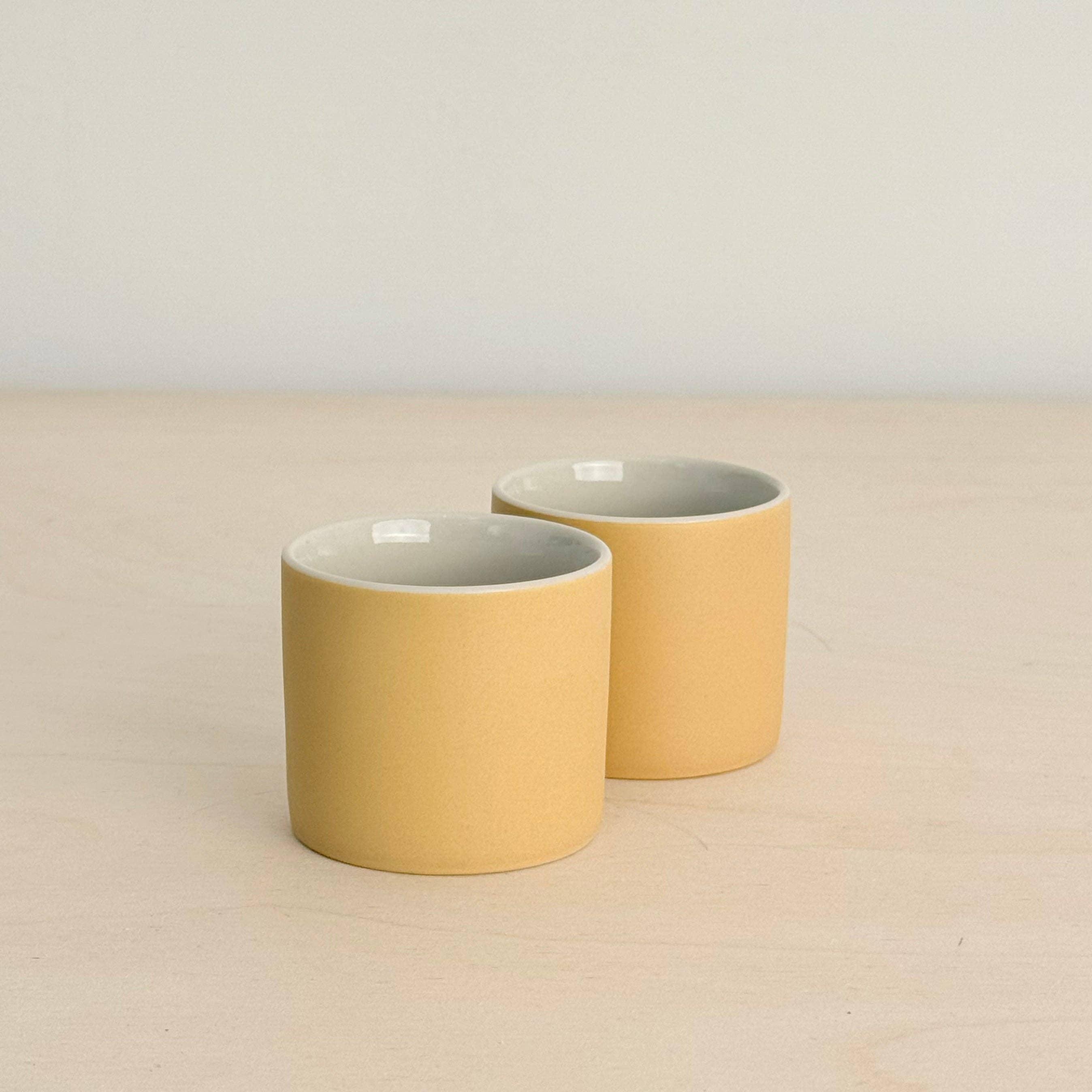 Mion Mug set of two, ceramic mugs in matte yellow finish on light wood surface