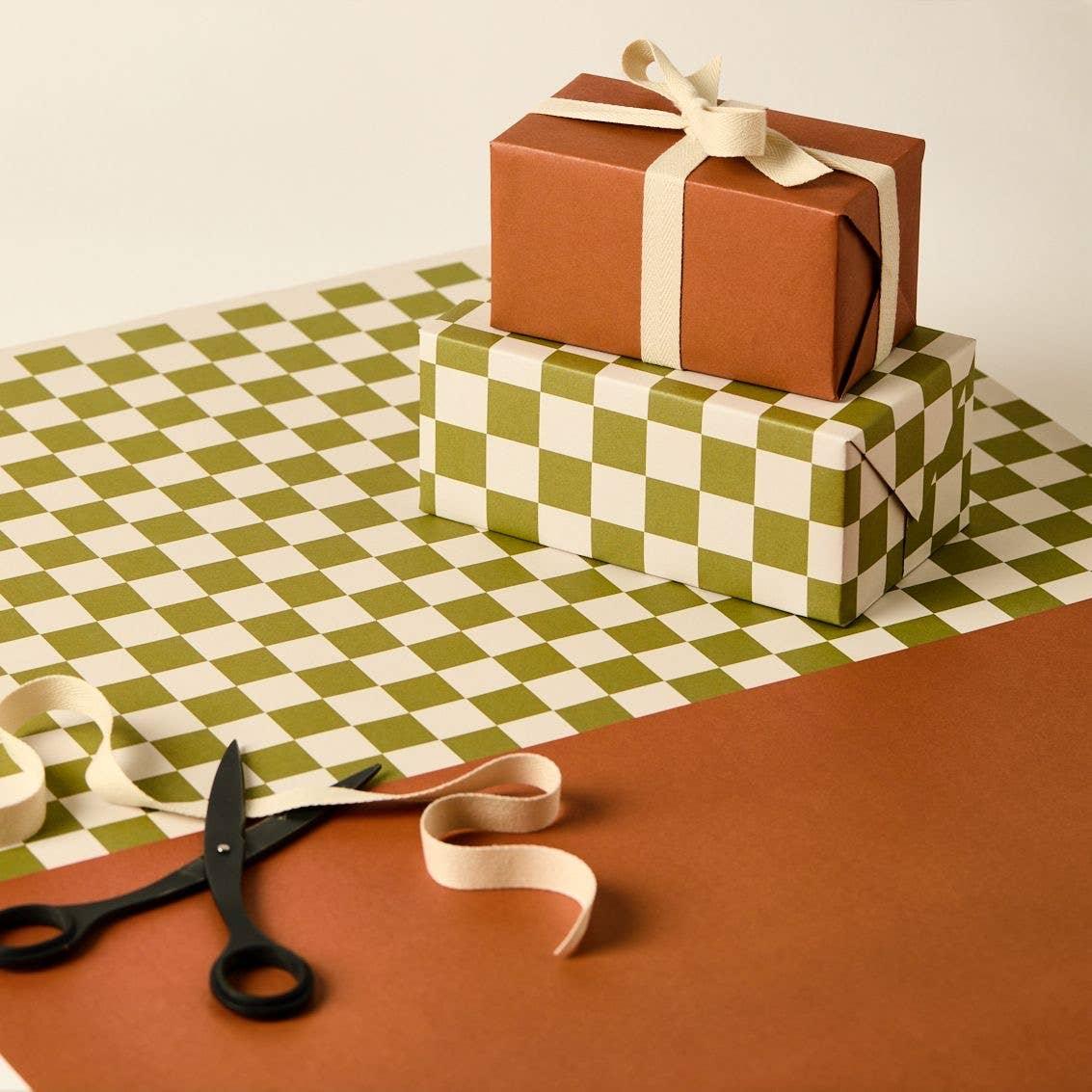Ola Studio gift wrap with green checkered and rust paper, cotton ribbon, black scissors.