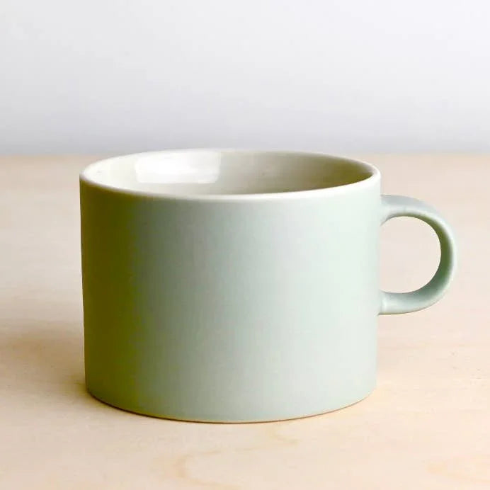 Kinto pale green ceramic mug with handle on light wood surface
