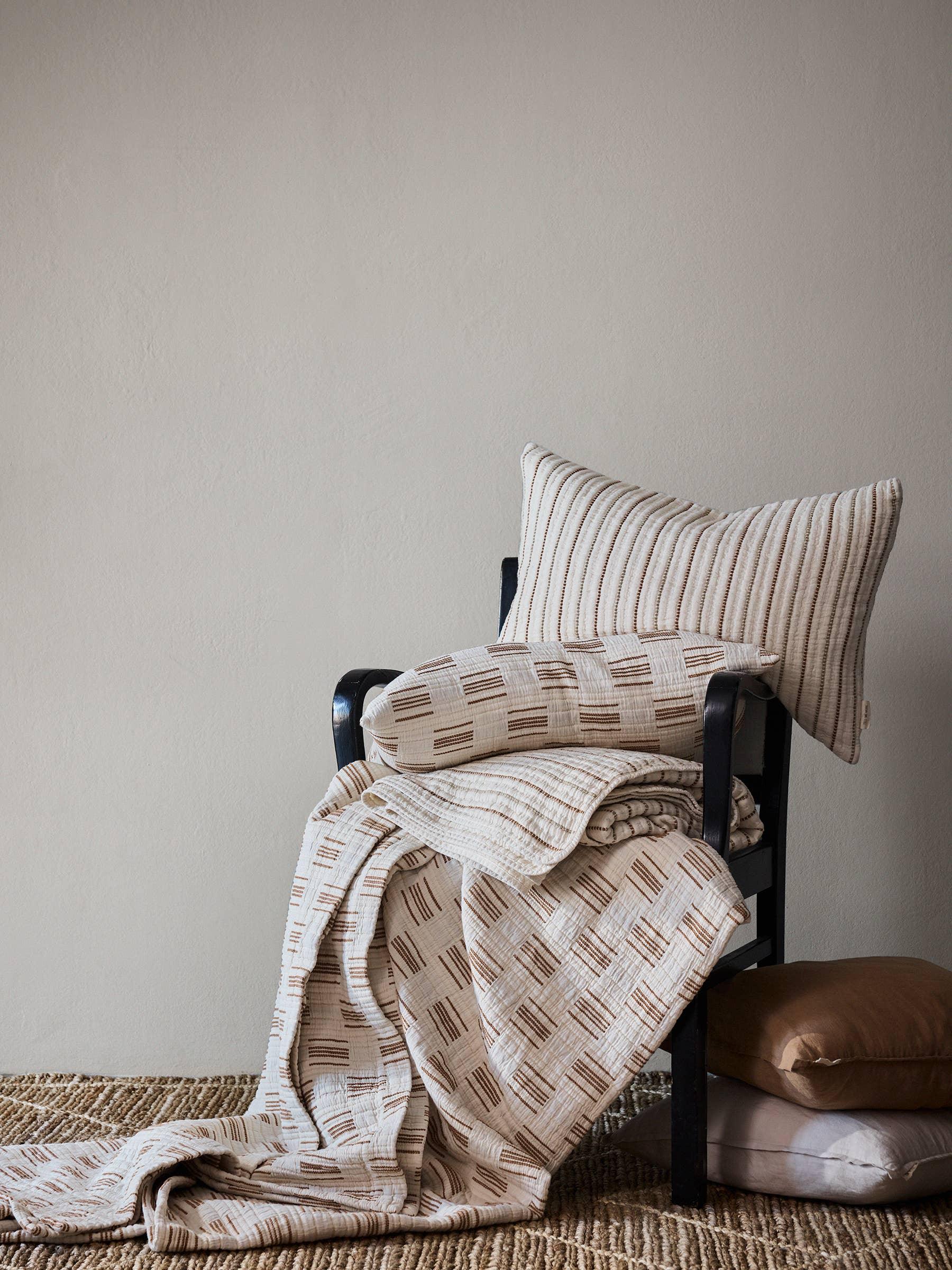 Ferm Living cotton striped and patterned beige quilt and cushions on black chair
