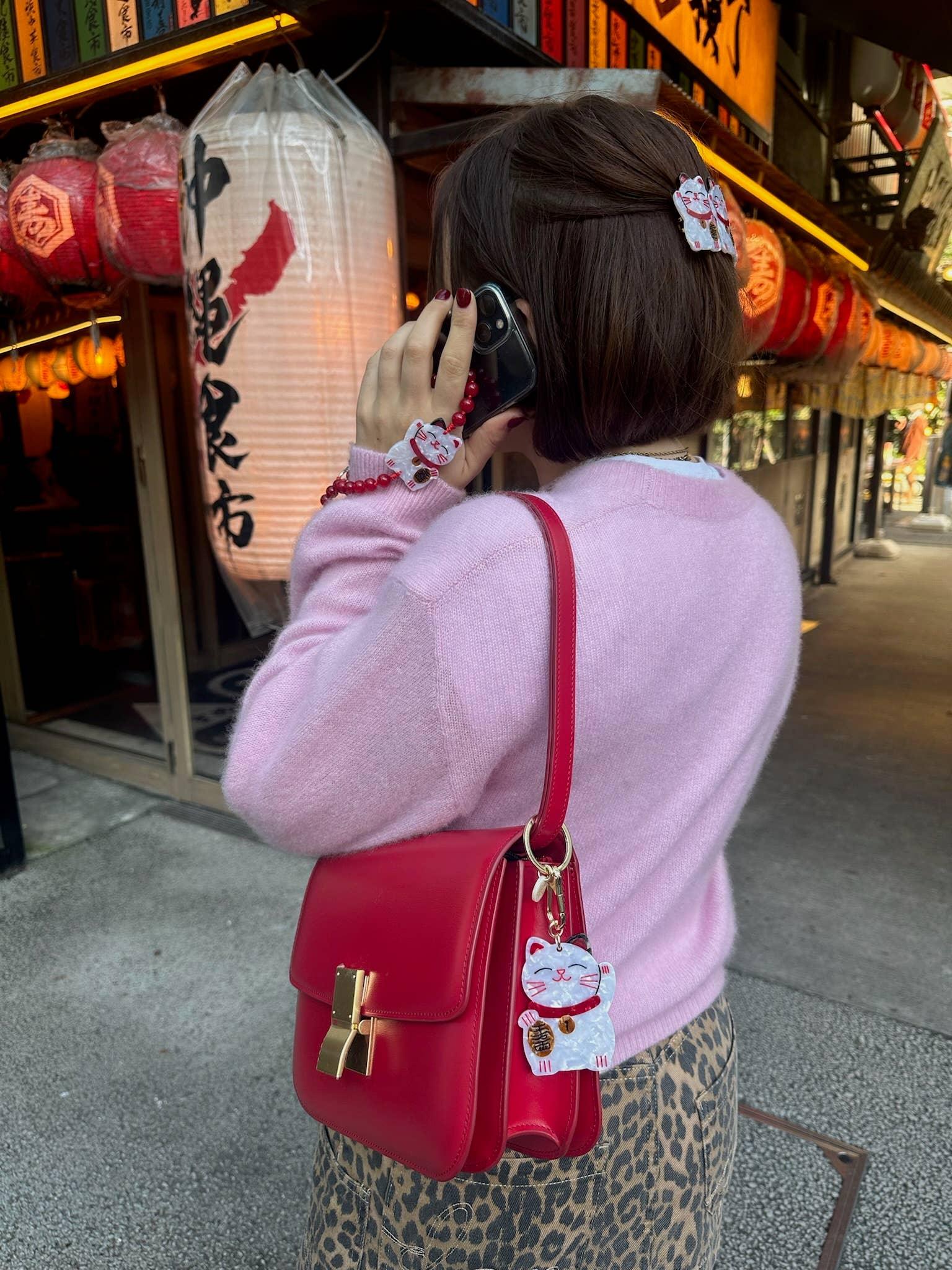 Mochi La Vie Maneki Neko acrylic keychain, hair clip, and charm on pink sweater and red leather bag
