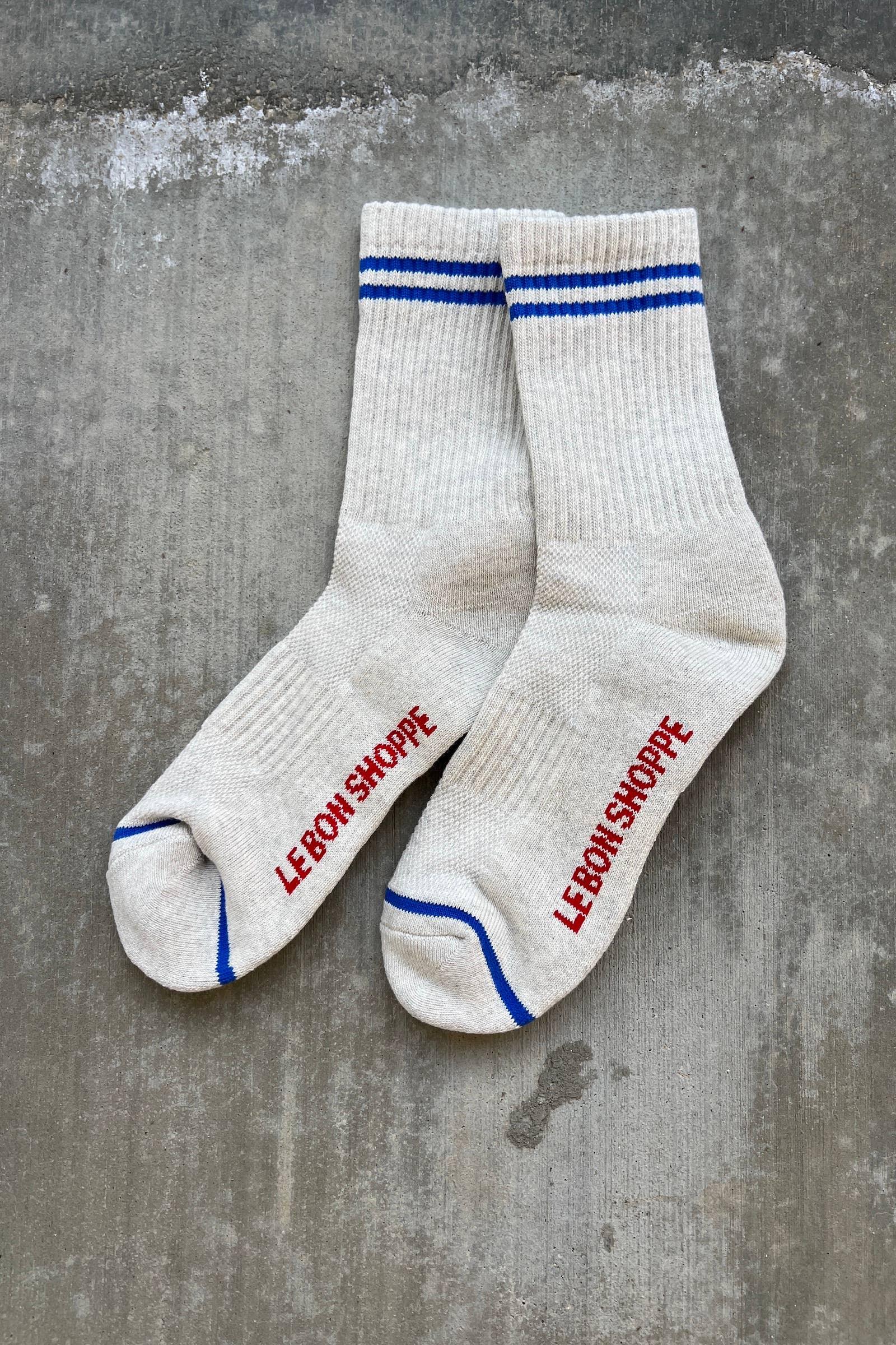 Le Bon Shoppe cream cotton socks with blue stripes and red logo lettering on concrete