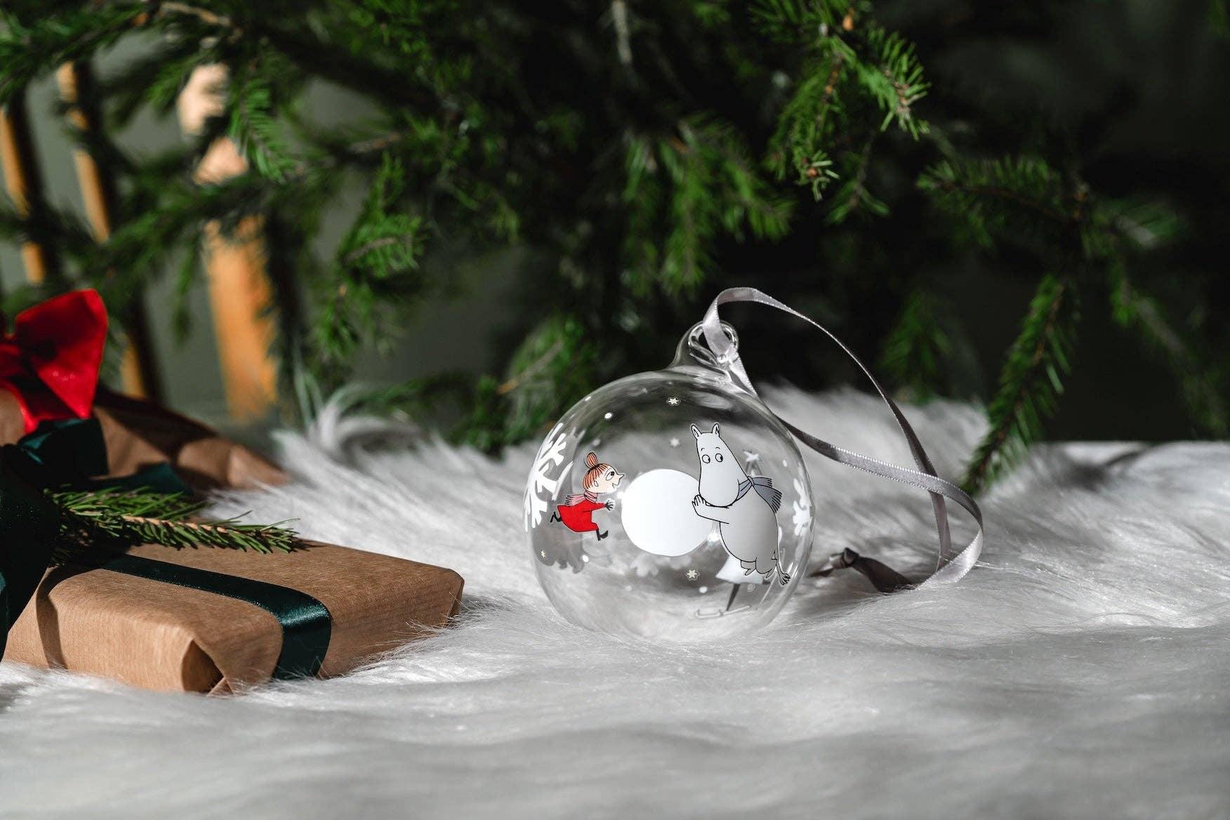 Moomin glass Christmas bauble with character illustration, clear ornament on fur by tree