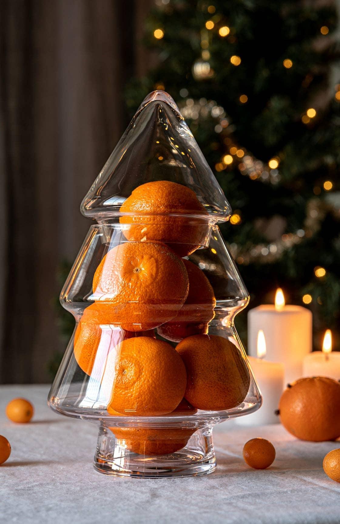 Clear glass Christmas tree jar filled with fresh oranges on a festive table setting.
